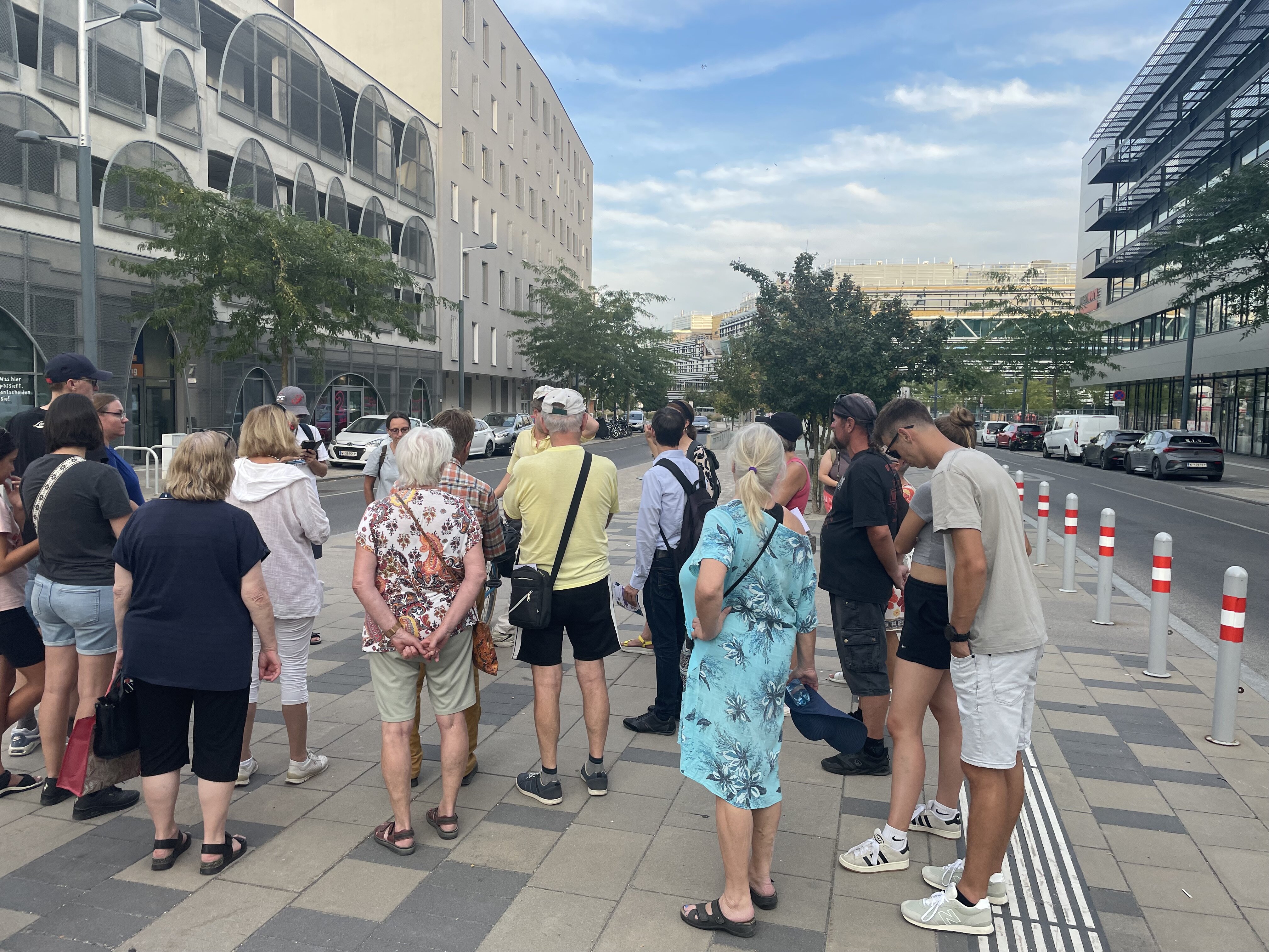 viele Personen die in der Seestadt stehen und jemanden zuhören