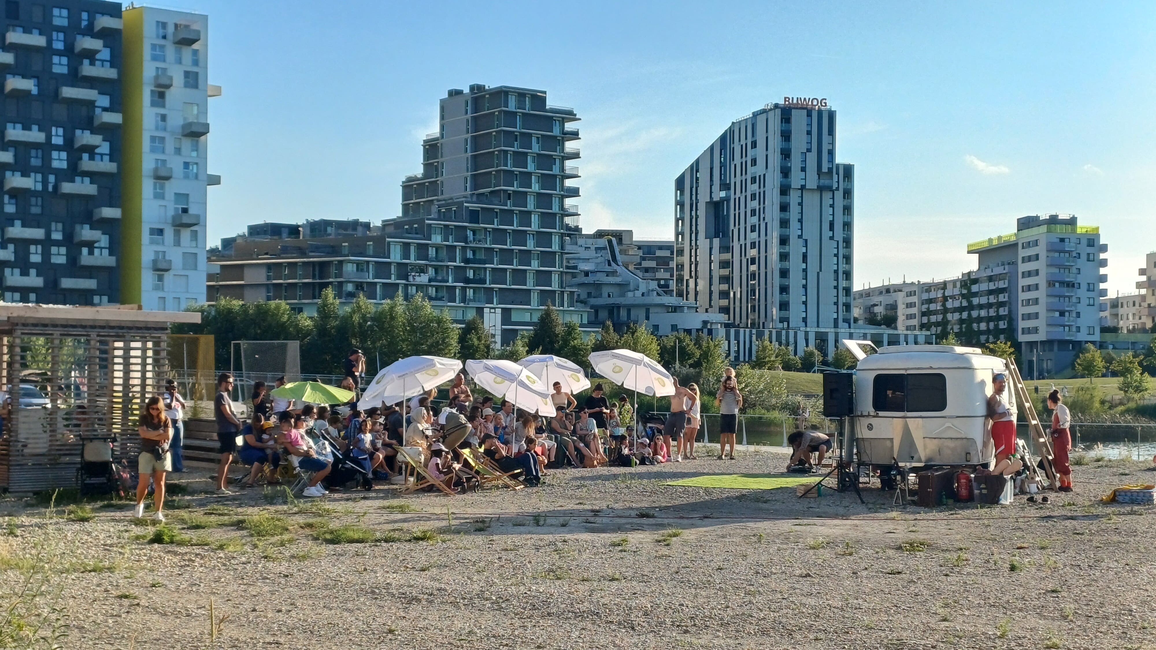 ein Wohnwagen steht auf Schotter, dahinter sind Hochhäuser
