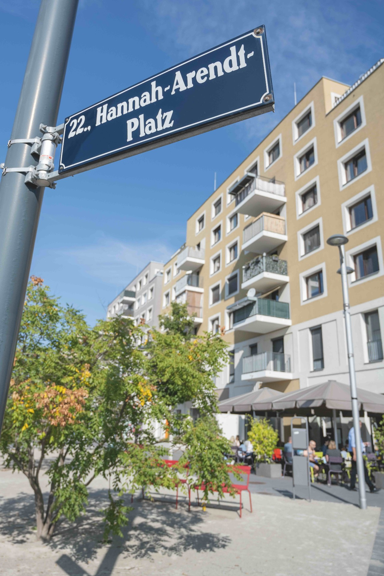 Straßenschild Hannah Arendt Platz mit Baum und Gebäude im Hintergrund