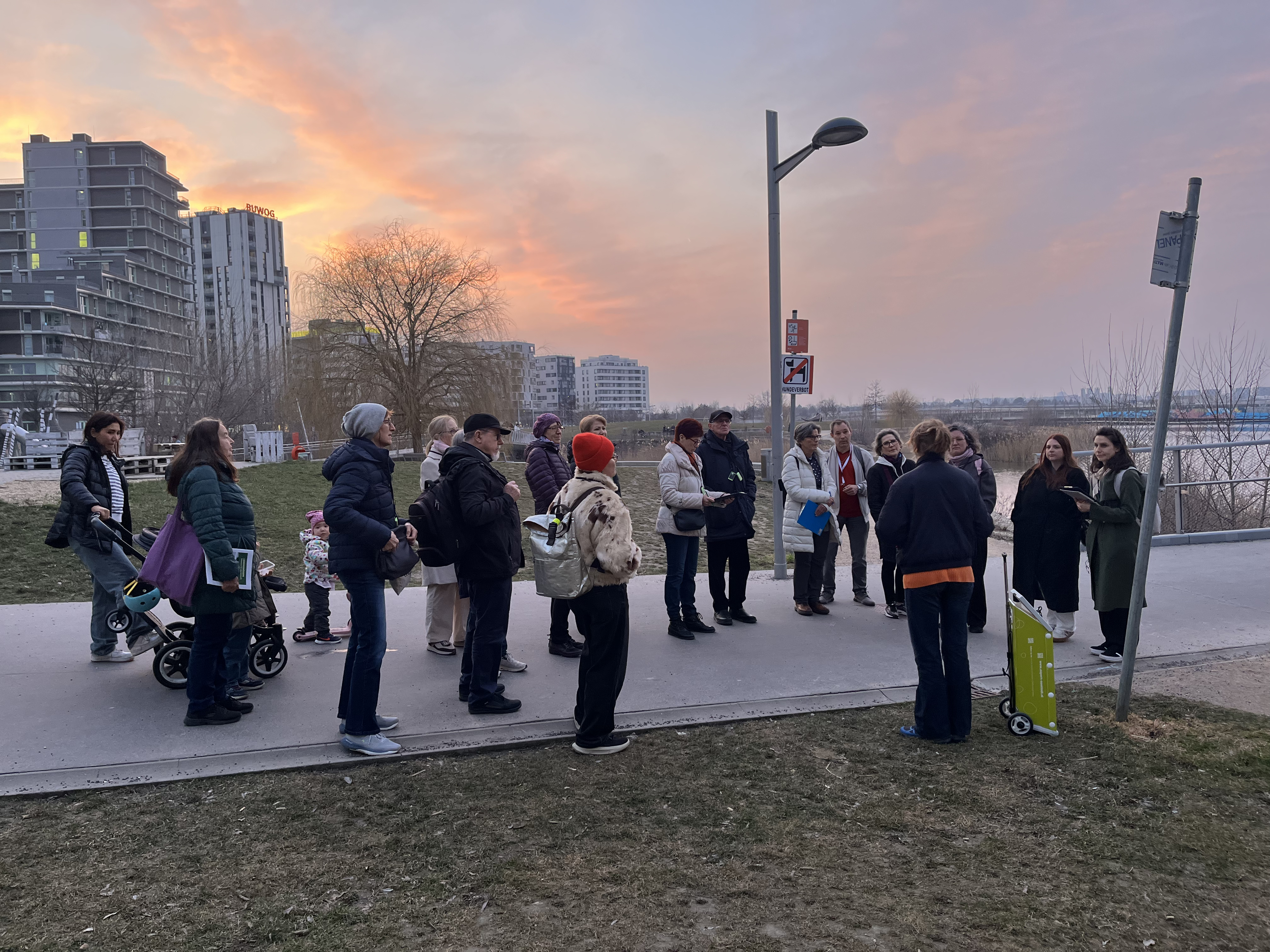 Gruppe steht bei Führung am Jane Jacobs Steg mit Sonnenuntergang im Hintergrund
