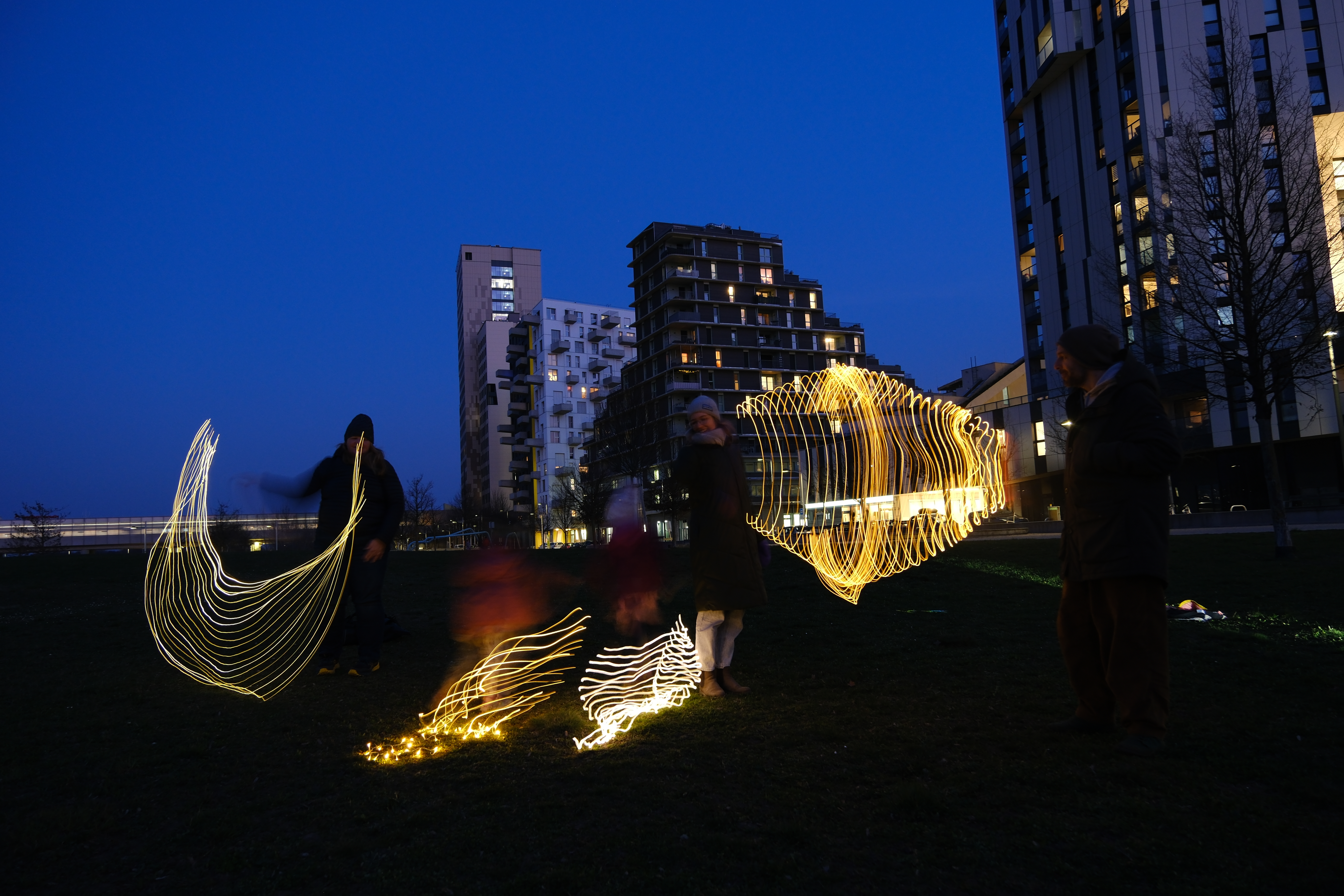 Menschen spielen mit Lichtquellen und erzeugen bei Dämmerung durch Langzeitbelichtung verschiedene Lichtermuster, die Menschen stehen auf einer W