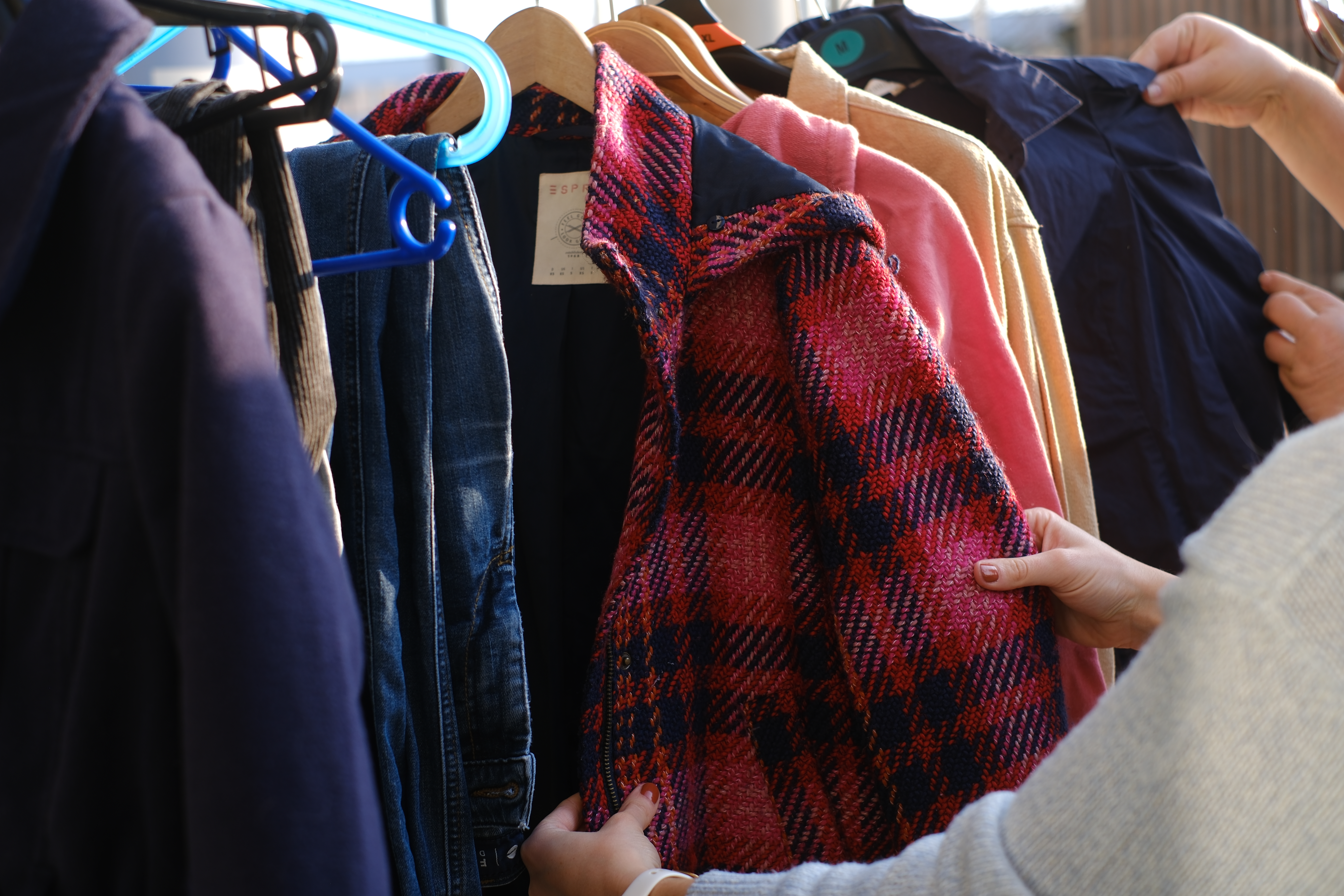 Kleidungsstücke auf einer Kleiderstange und zwei Personen, die sich die Kleidung ansehen