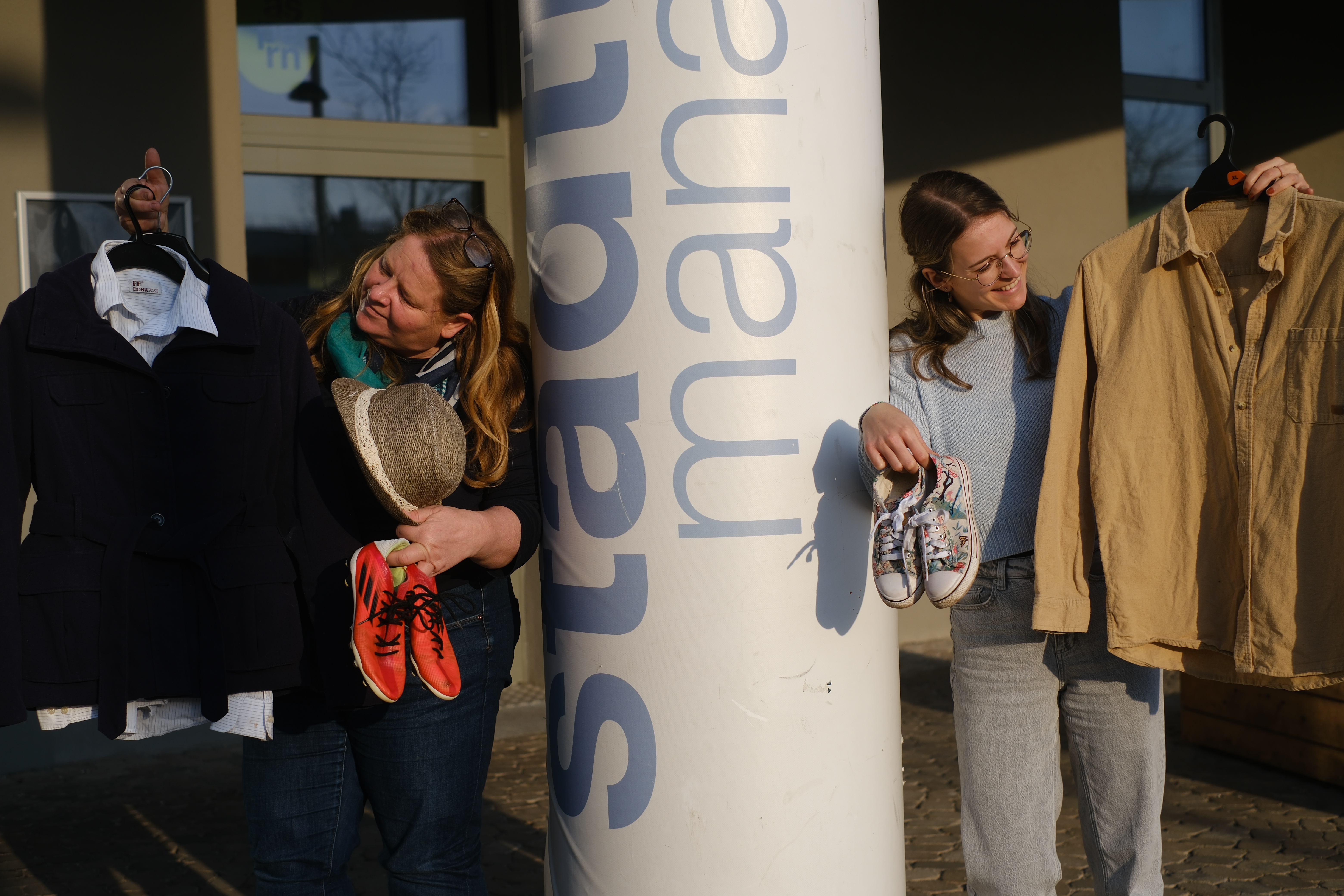 Zwei Personen, die Kleidung und Schuhe halten vor dem Staddteilmanagement Büro
