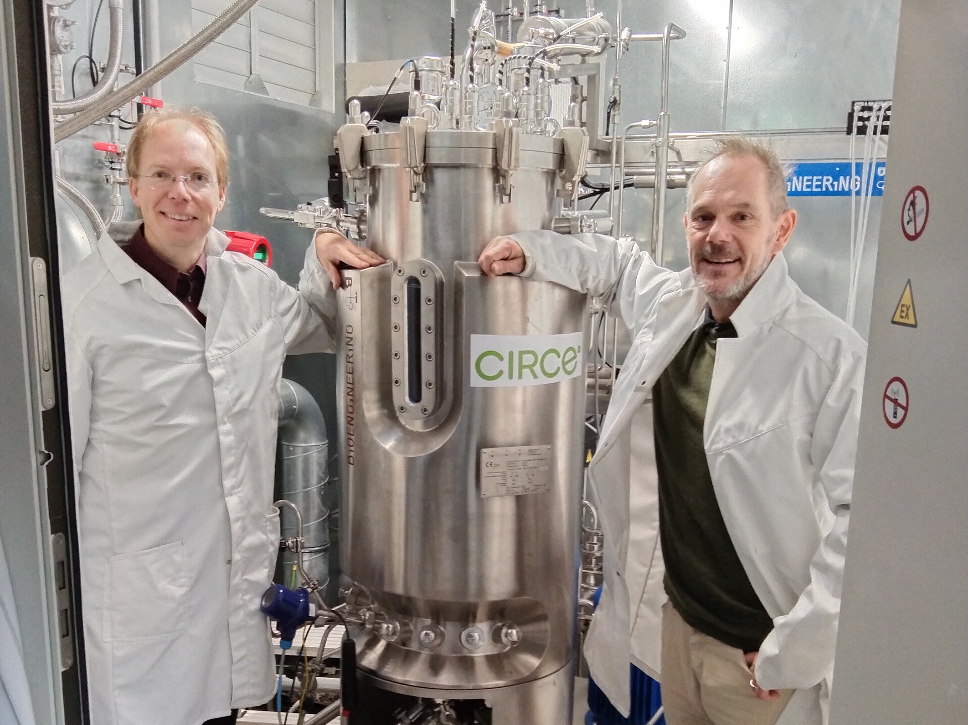 Zwei Männer in Laborkitteln - in der Mitte ein Gasreaktor