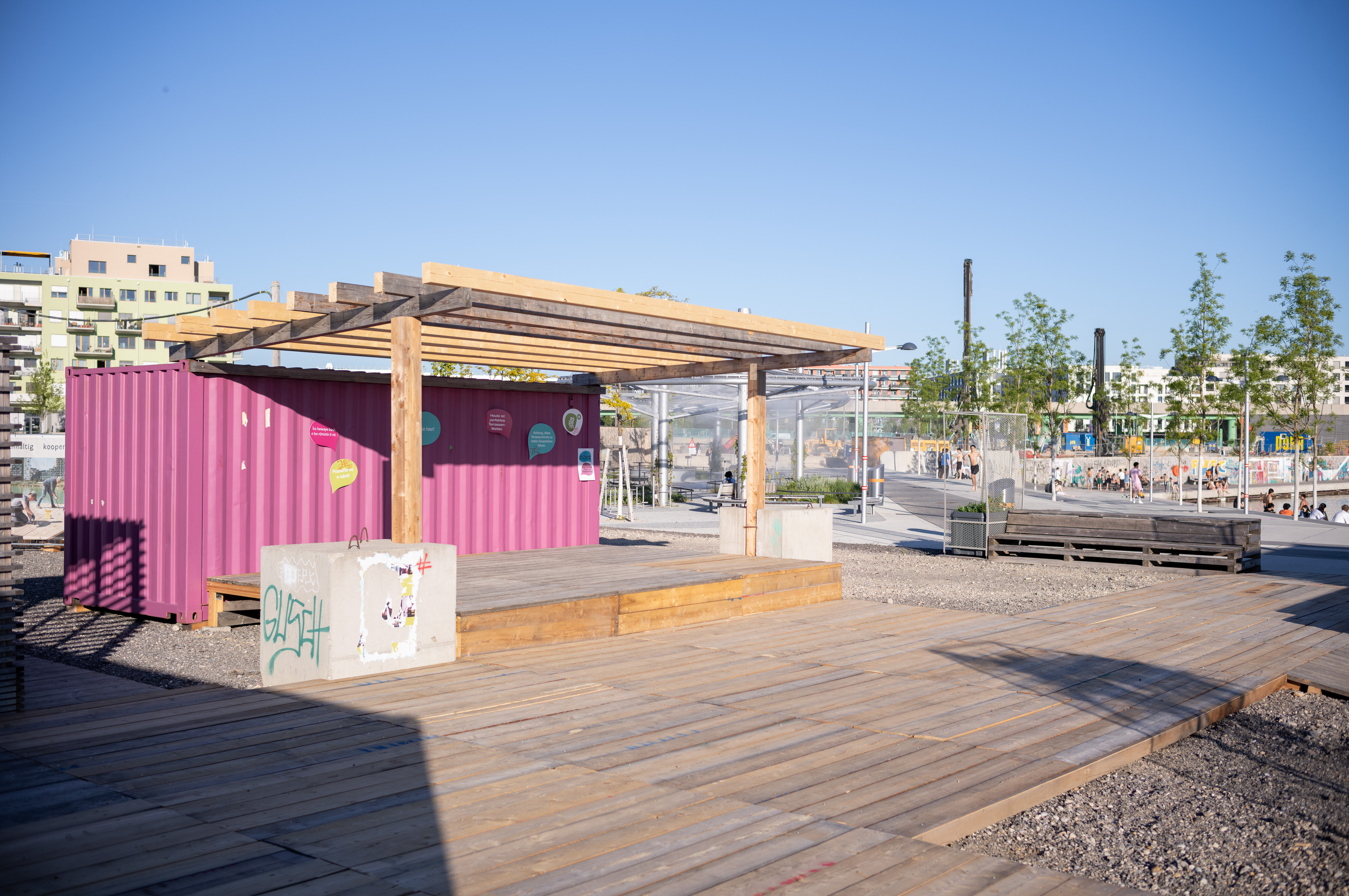 Eine Holzterrasse mit einem pinken Container und einem Vordach
