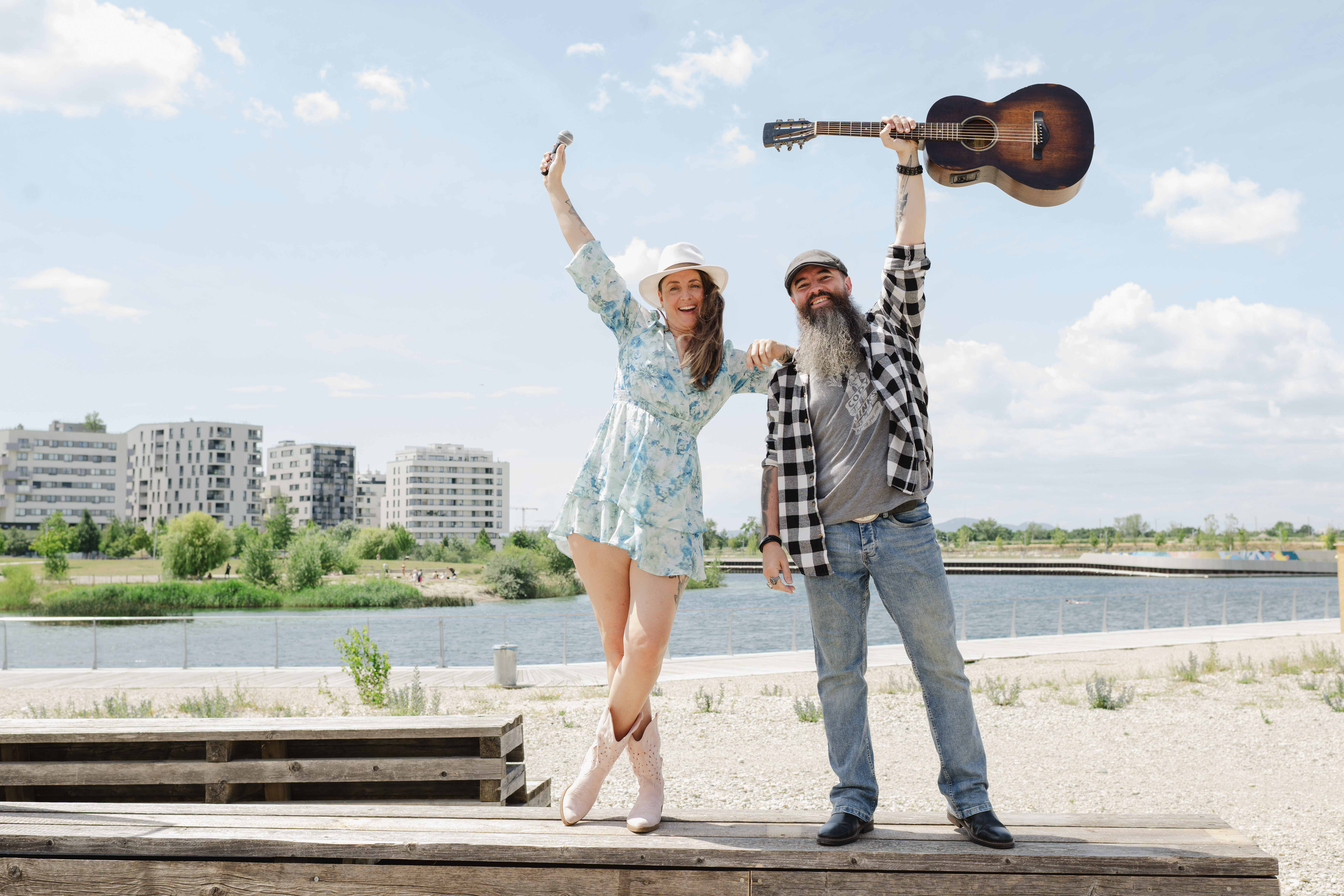 Zwei Personen halten ein Mikrofon bzw. eine Gitarre in die Höhe, Hintergrund See