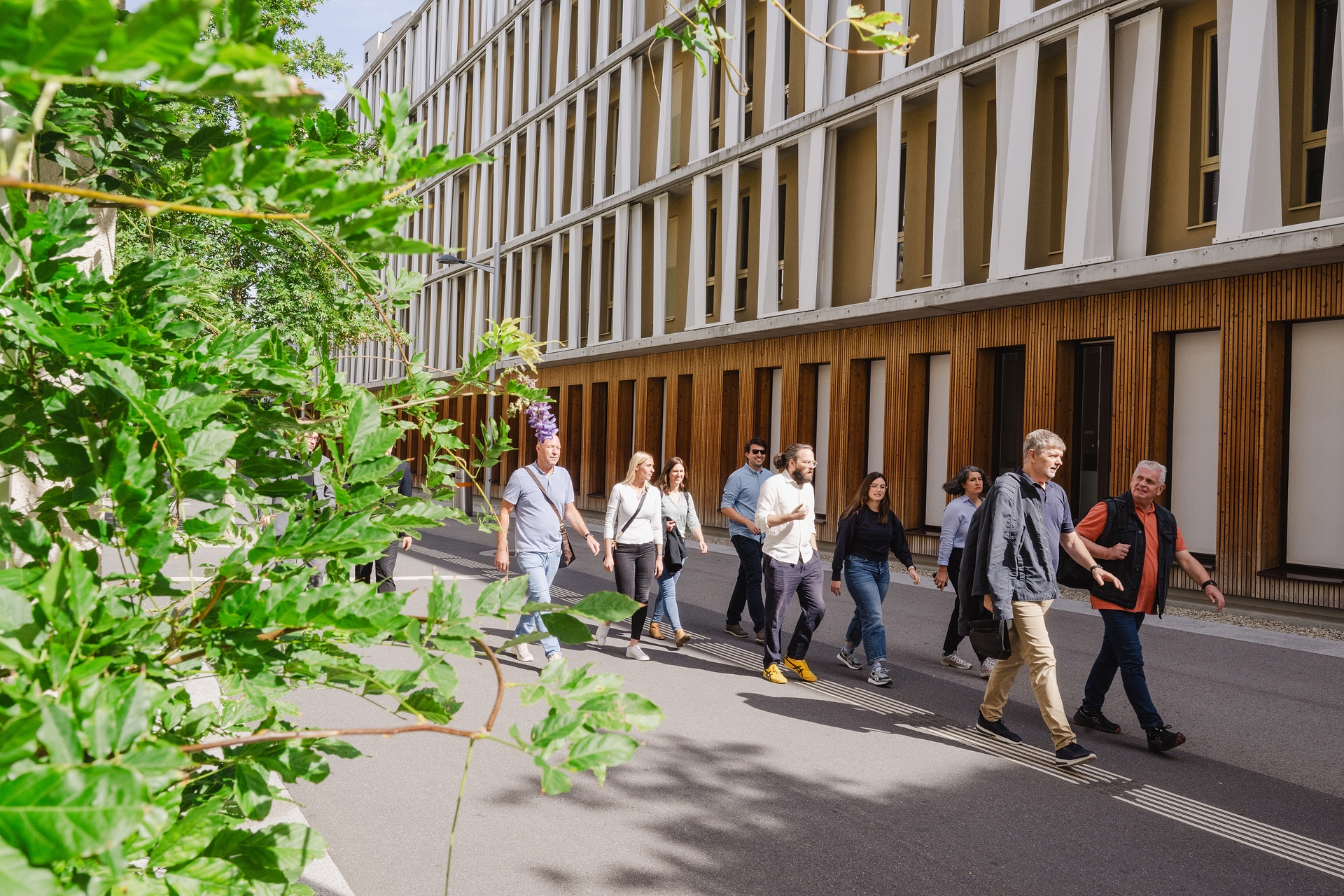 Mehrere Personen gehen auf einem Platz, modernes Gebäude im Hintergrund