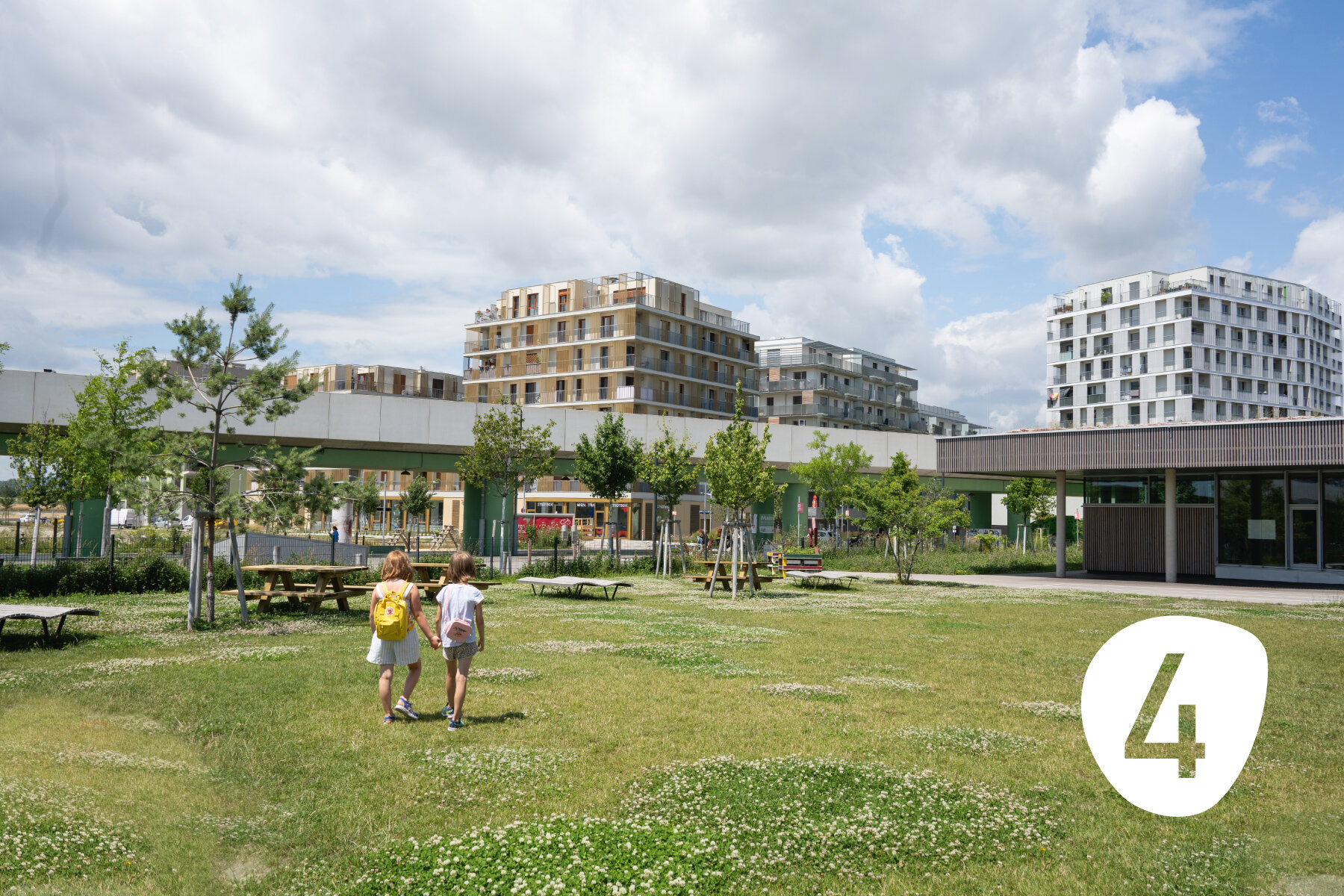 zwei Linder gehen über einen blühenden Park an einer U-Bahn Richtung moderner Wohnhäuser