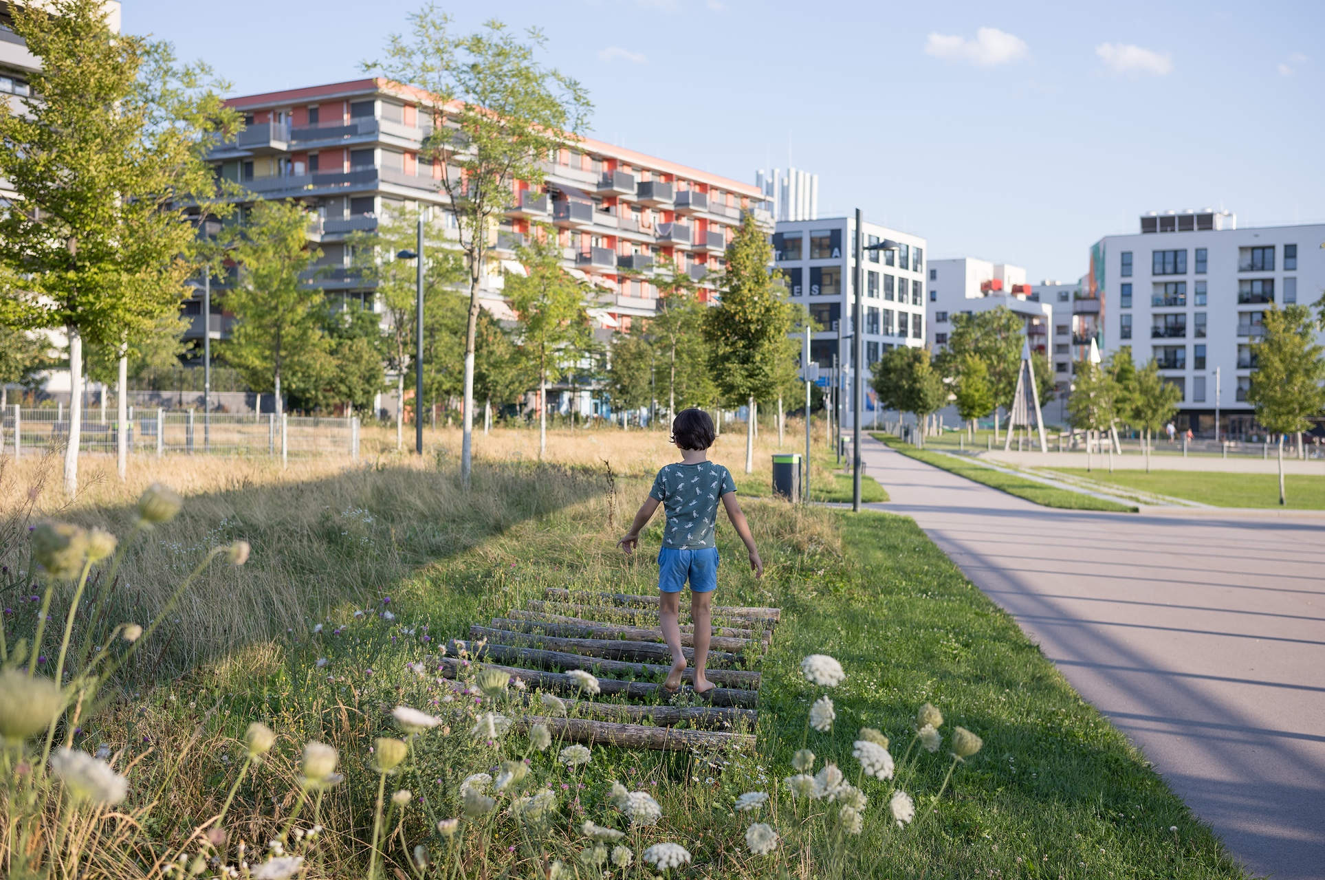 aspern Seestadt vereint Generationen. Kind von hinten in einem naturnahen Park mit Gebäude im Hintergrund.