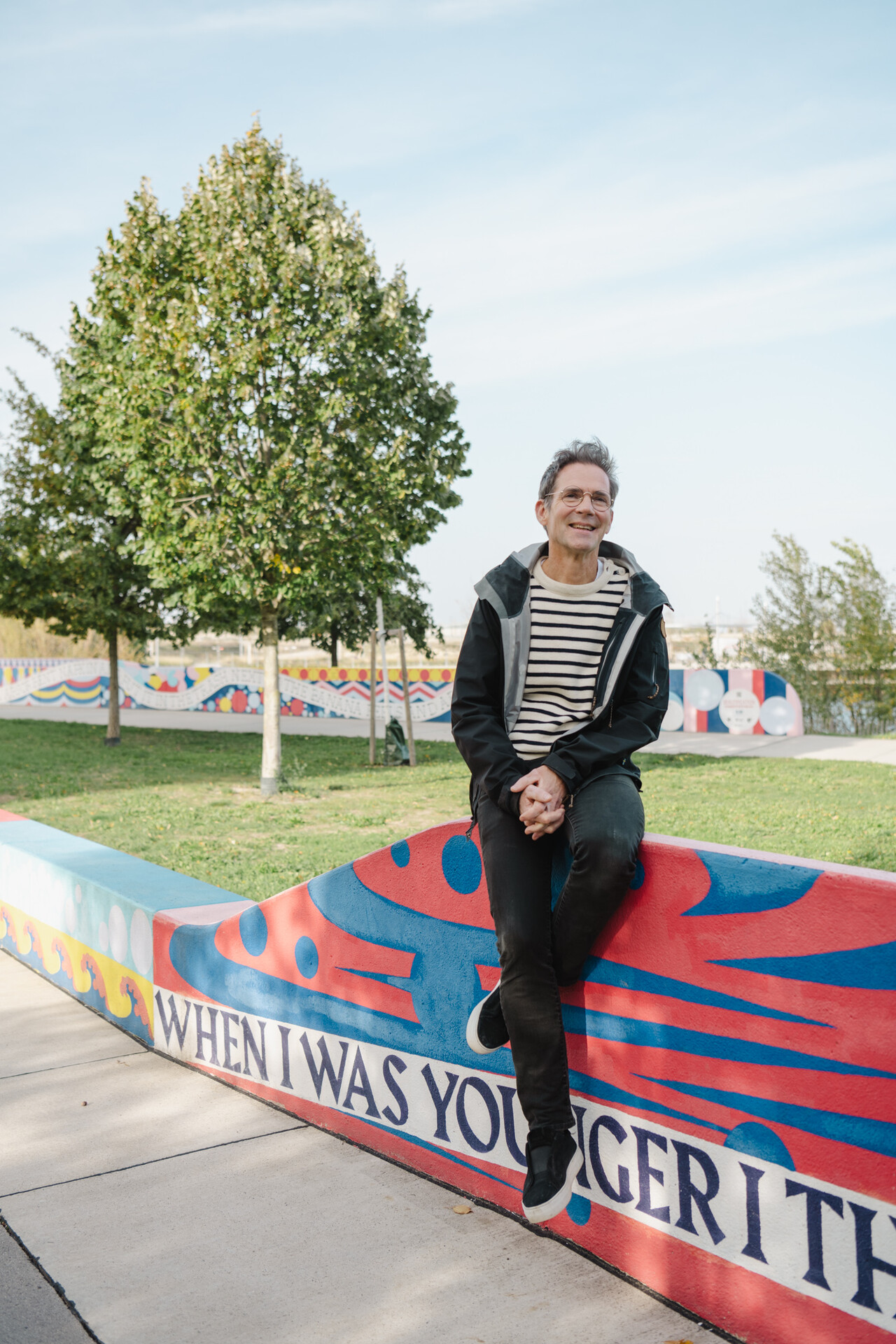 Johannes Tovatt ist der Masterplaner für die Seestadt. Ein lächelnder Mann auf einer Wand, im Hintergrund Park.