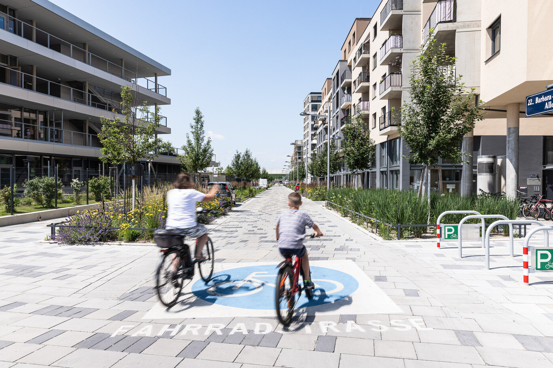 Eine breite Fahrradstraße in der Seestadt, gesäumt von modernen Wohngebäuden und Grünstreifen, zwei Personen fahren mit dem Rad durch die verkehrsberuhigte Allee.