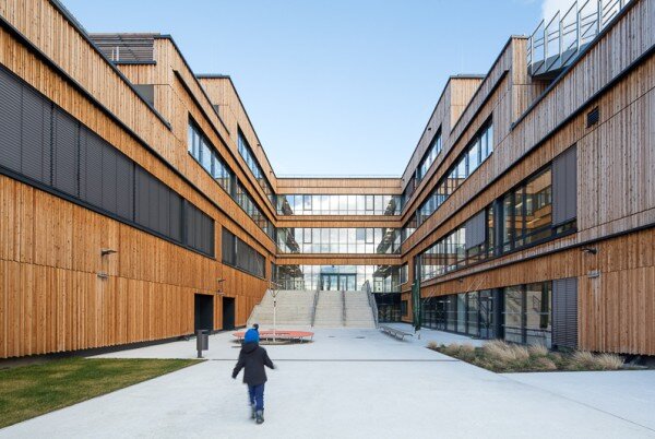 Campus Seestadt Kind läuft in einen offenen Innenhof eines modernen Schulgebäudes mit Holzfassade und großen Fenstern.