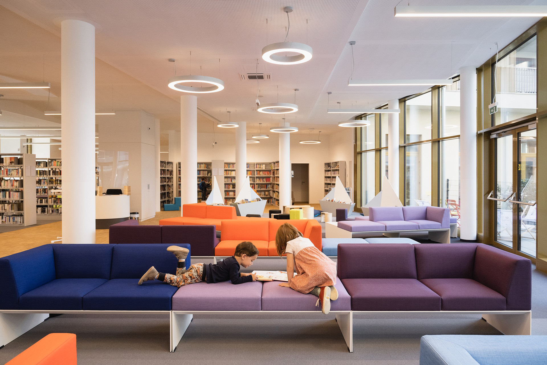 Die Bücherei Seestadt lädt zum Bücher entdecken. Zwei Kinder lesend auf modernen Möbeln in einer Bücherei.