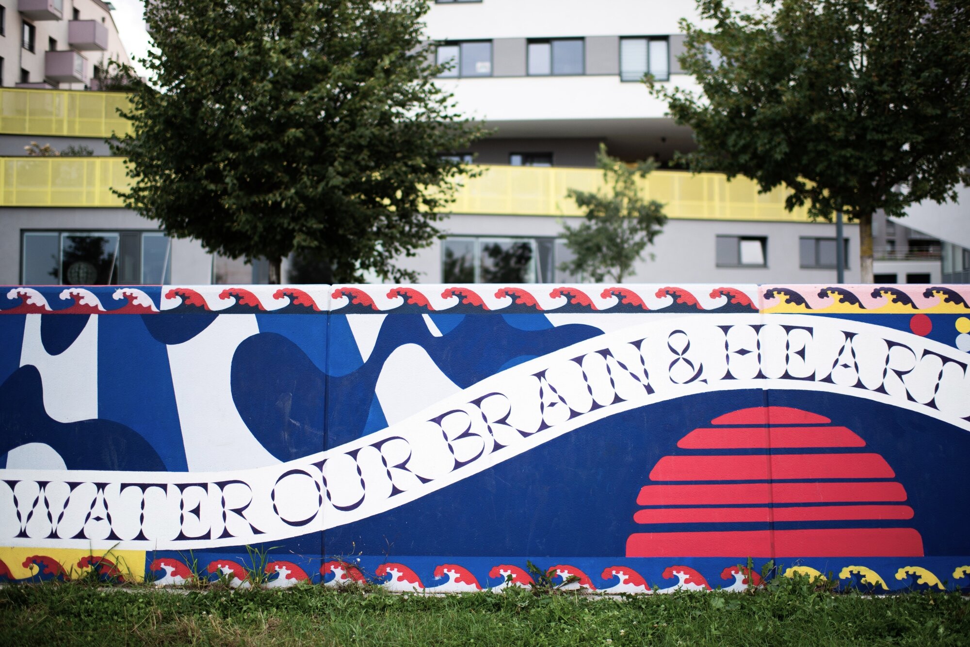 bunt bemalte Wand mit Designs von Stefan Sagmeister vor Bäumen und Wohngebäuden