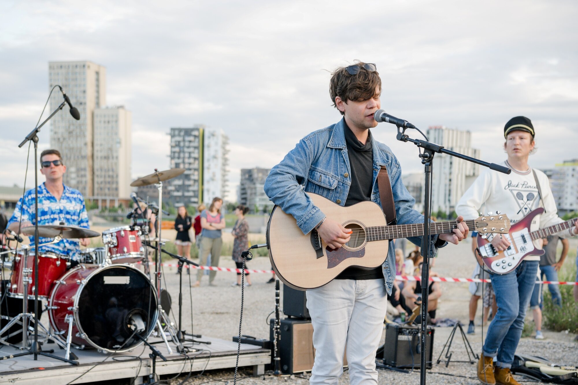Nino aus Wien und Band spielen auf einem Baufeld vor der Skyline der Seestadt