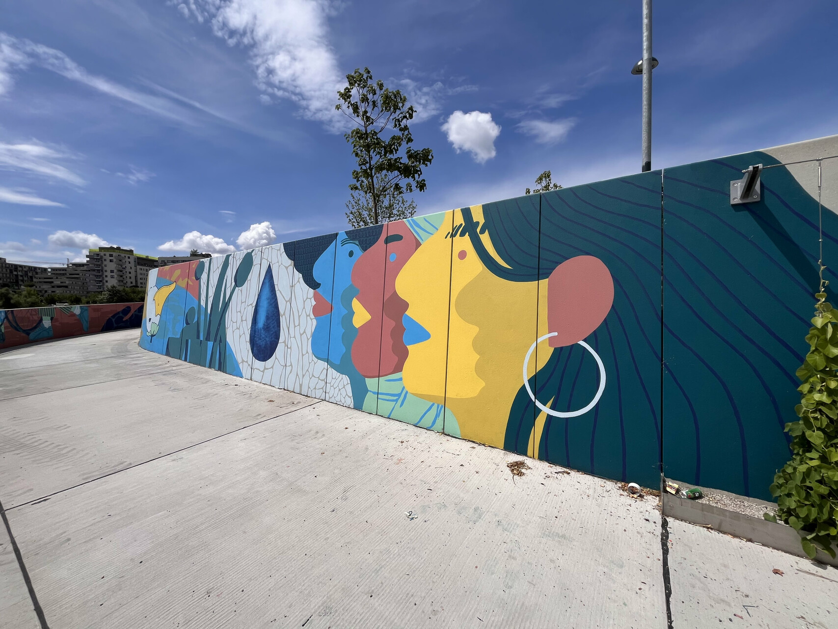 Buntes Mural an einer Promenade, davor die Promenade, weit im Hintergrund ein paar Häuser