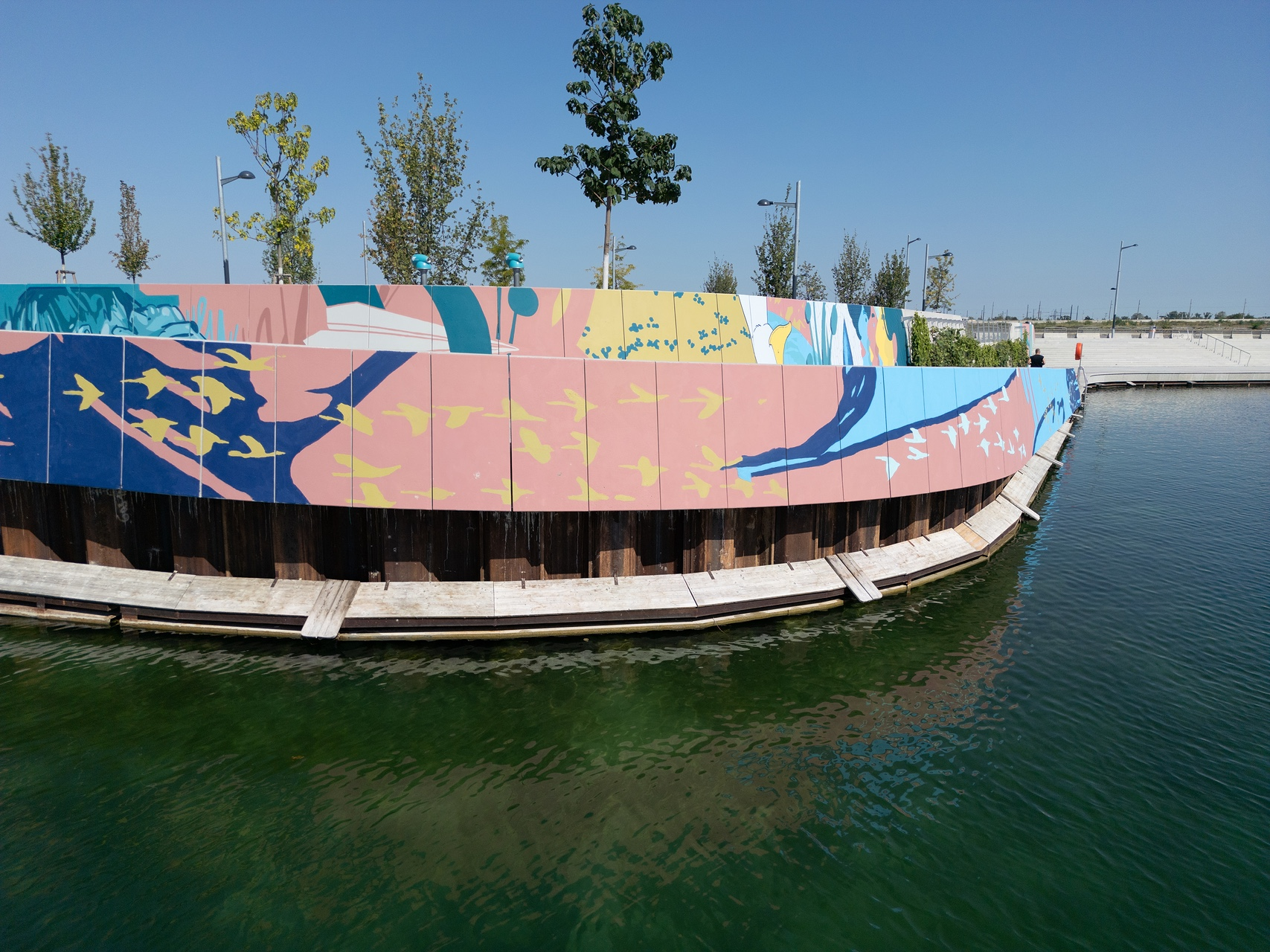 Buntes Mural an der Promenandenwand, davor der See, rechts sind Stufen zu sehen