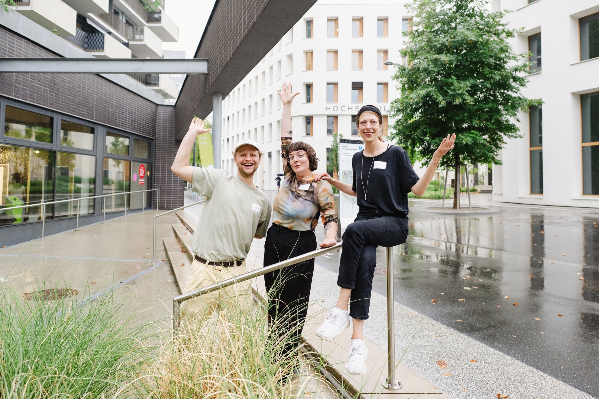 drei Personen von Stadtteilmanagement stehen und sitzen vor dem Eingang zu einem modernen Erdgescoßraum