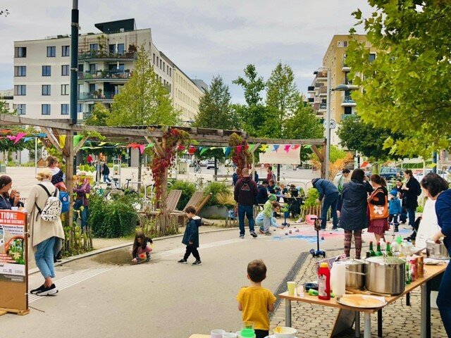 Blick auf einen Platz in der Stadt, es sind Stände zu sehen und Kinder und Erwachsene bewegen sich von Stand zu Stand