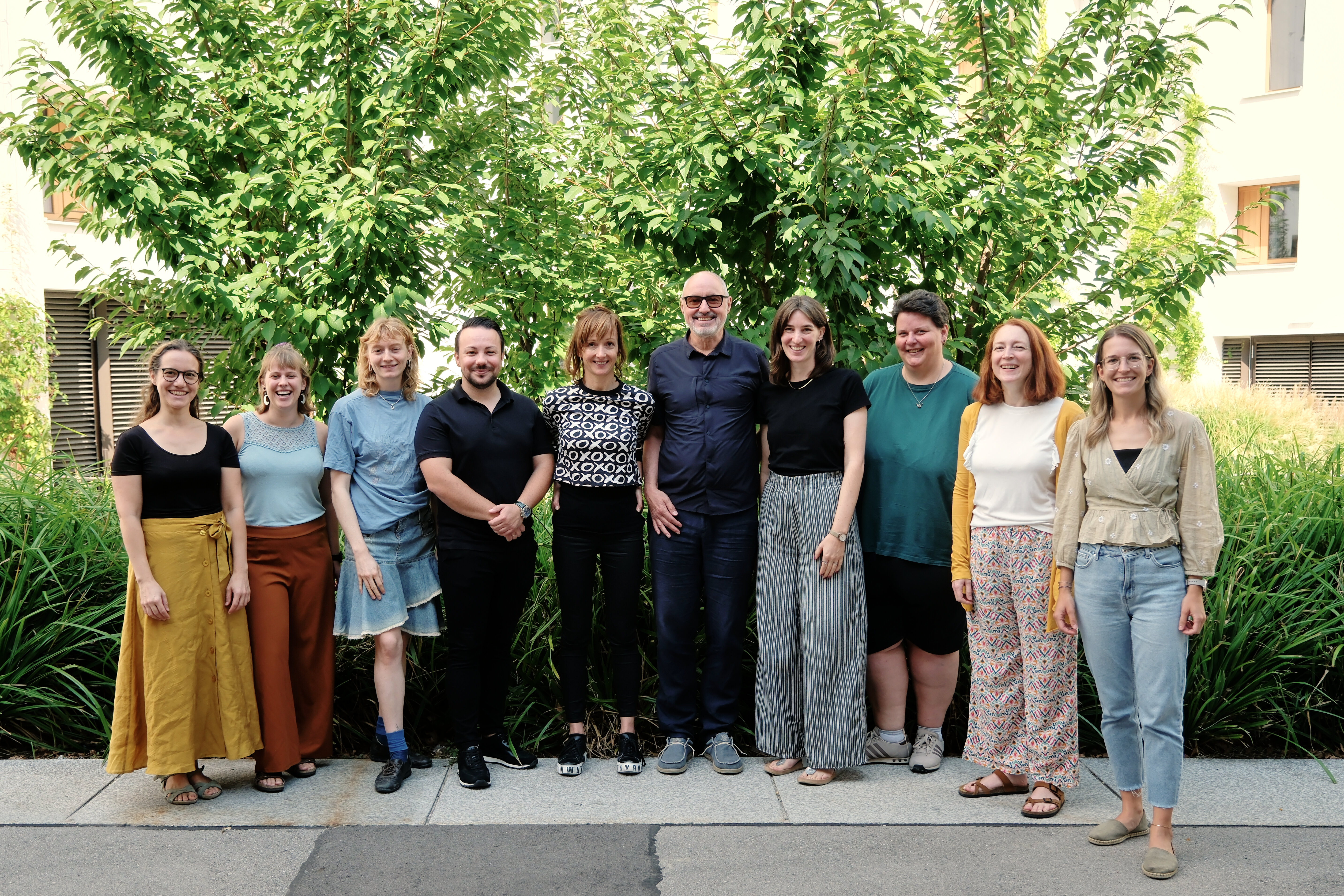 Teamfoto des Stadtteilmanagements Seestadt aspern vor einem begrünten Bereich in der Seestadt