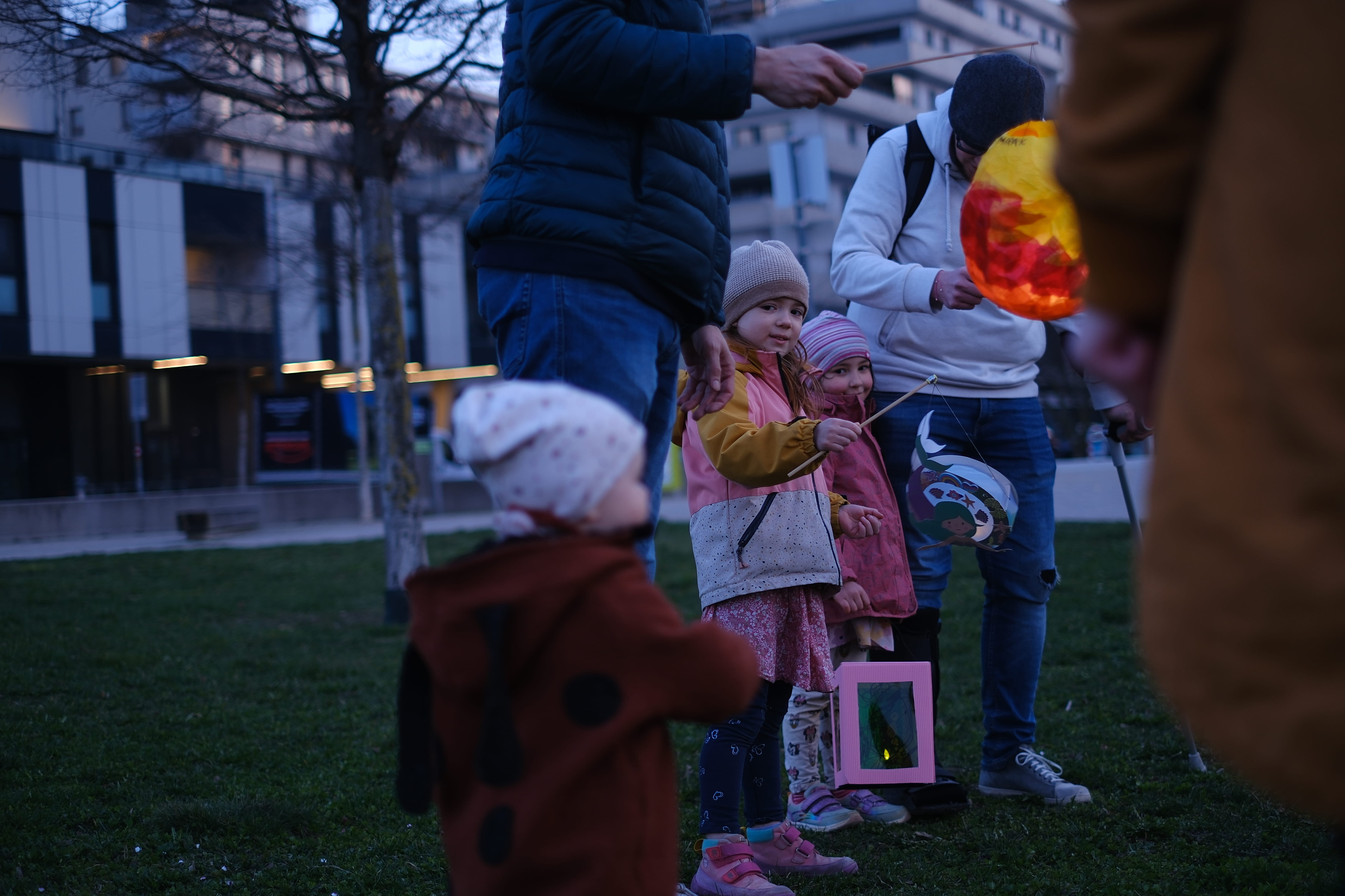 drei Kinder stehen umringt von Erwachsenen mit Laternen und schauen in die Höhe