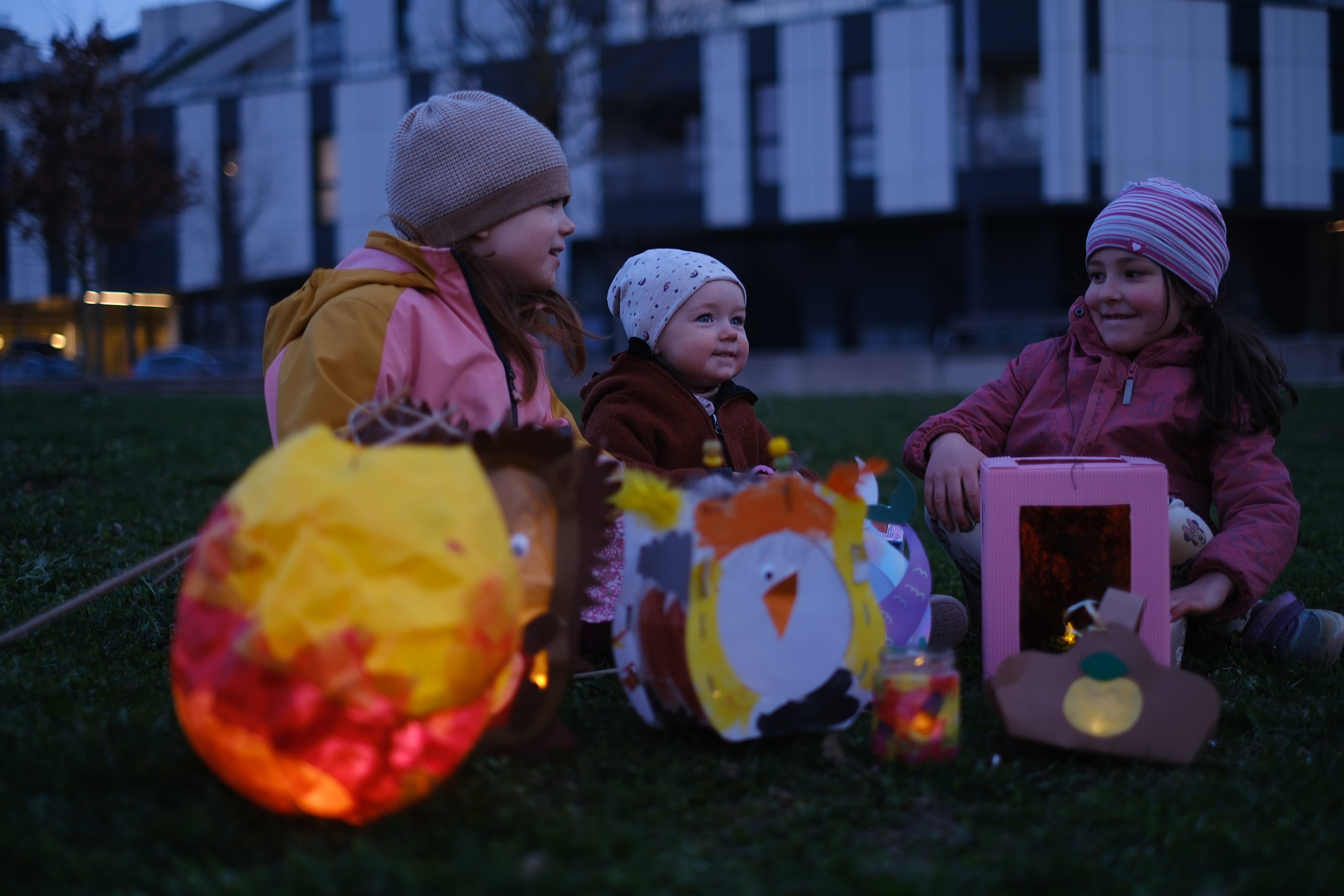 drei Kinder sitzen im Gras und leuchtende Laternen stehen vor ihnen
