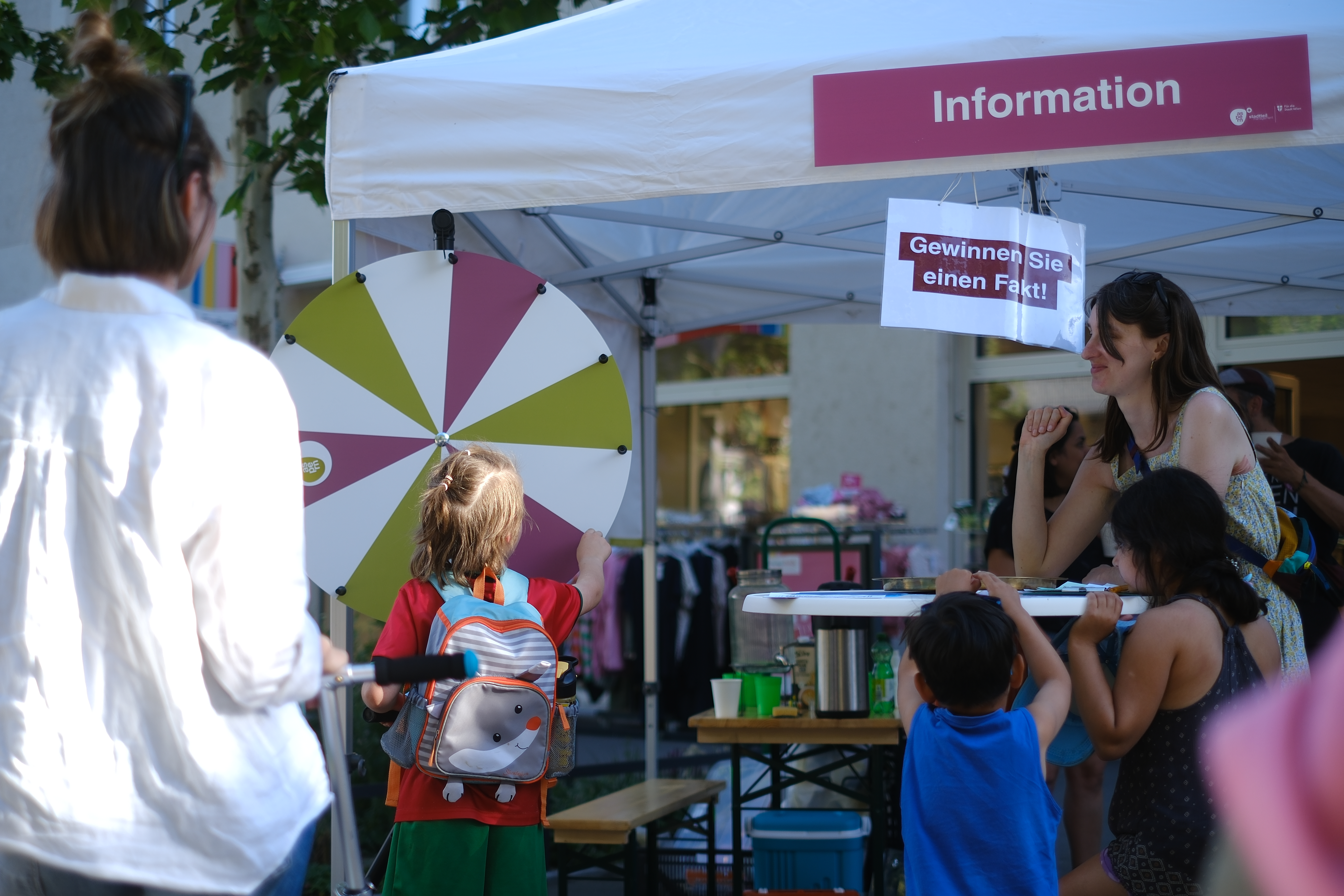 Ein Pavillon mit dem Schriftzug Information und darunter ein Glücksrad, an dem Personen drehen