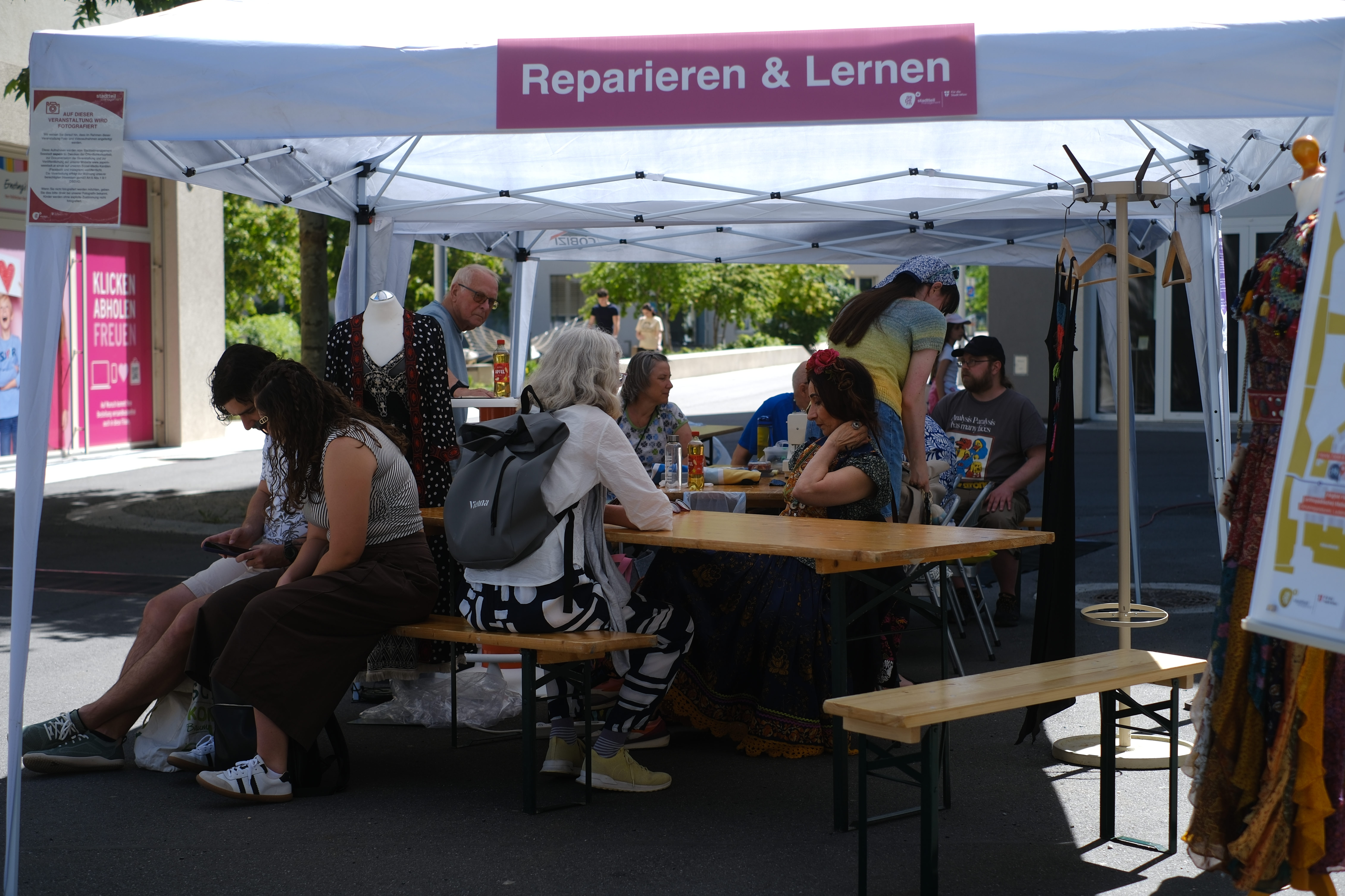 Personen sitzen auf einer Bank und unterhalten sich bei der Station Reparieren & Lernen