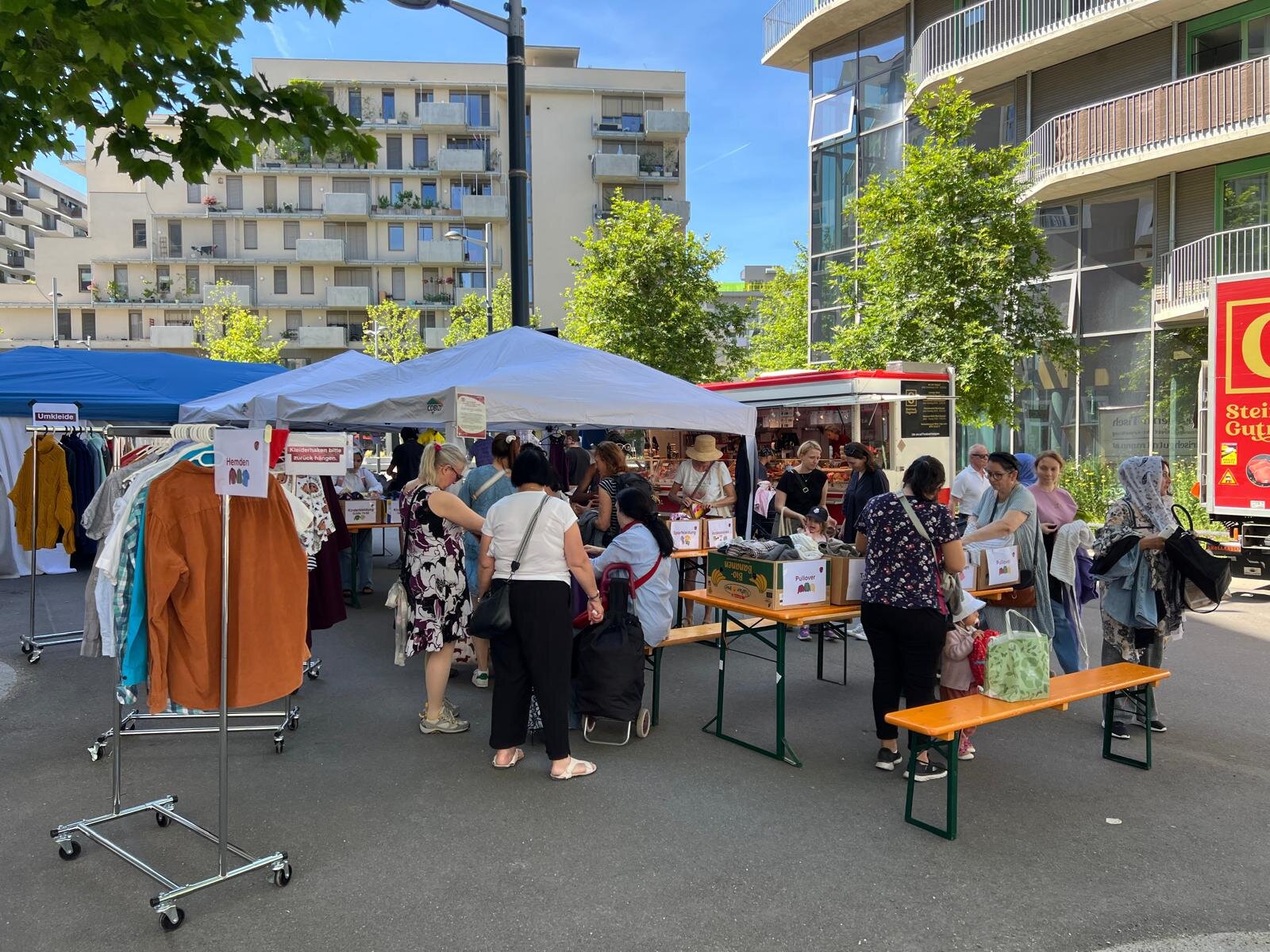 Personen auf einem Platz mit Pavillons und Kleiderstangen
