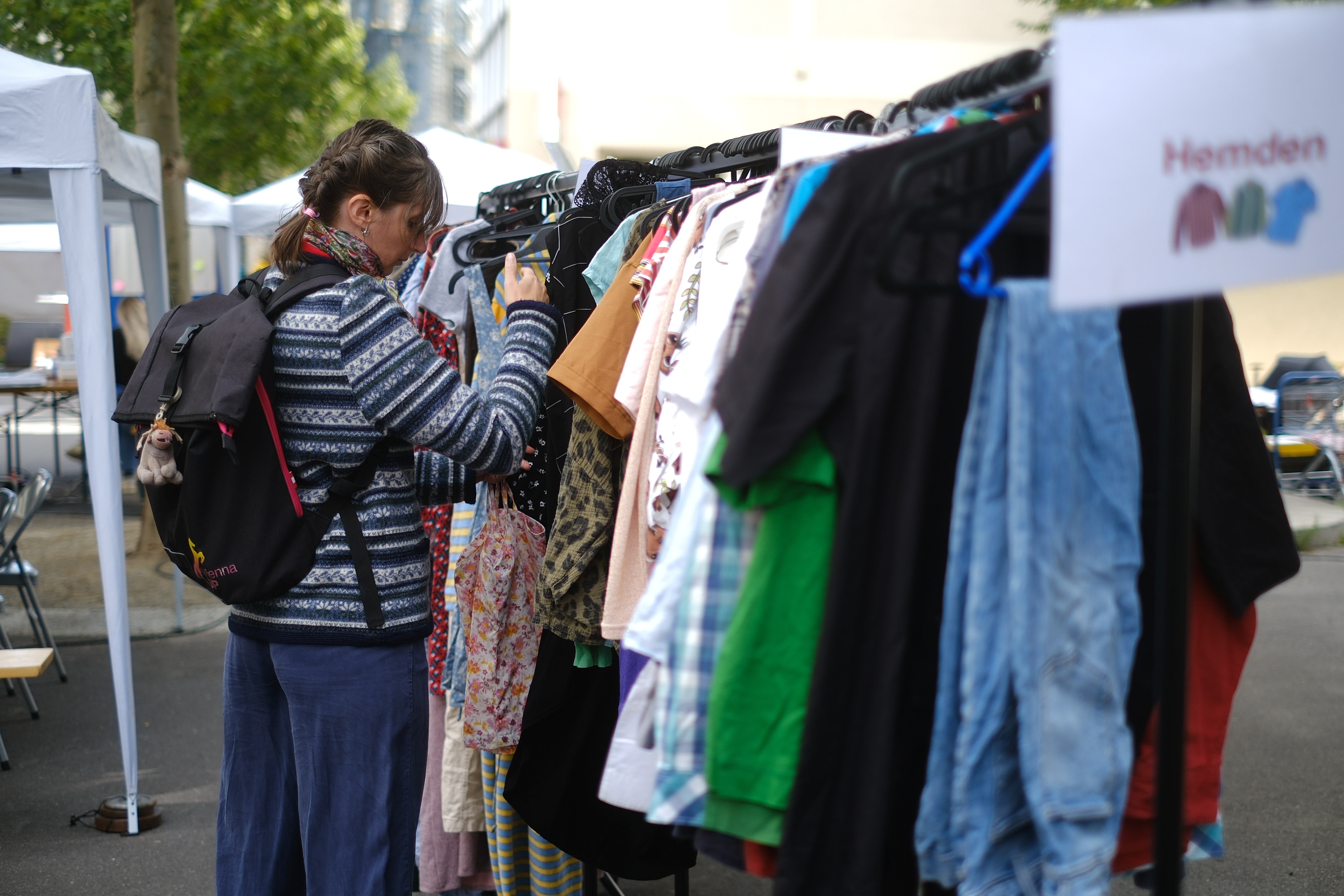 Frau stöbert durch Kleidung, die auf einer Kleiderstange aufgehängt ist