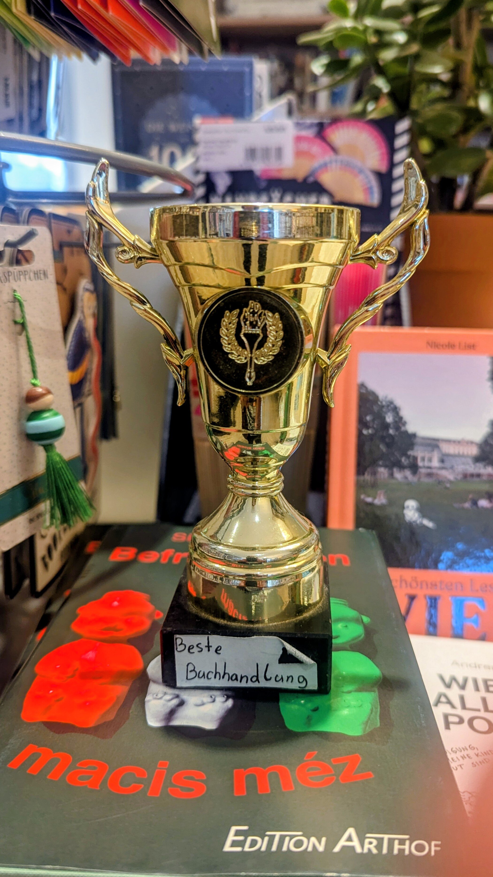 Ein goldener Pokal mit der Beschriftung "Beste Buchhandlung" steht auf einem Bücherstapel