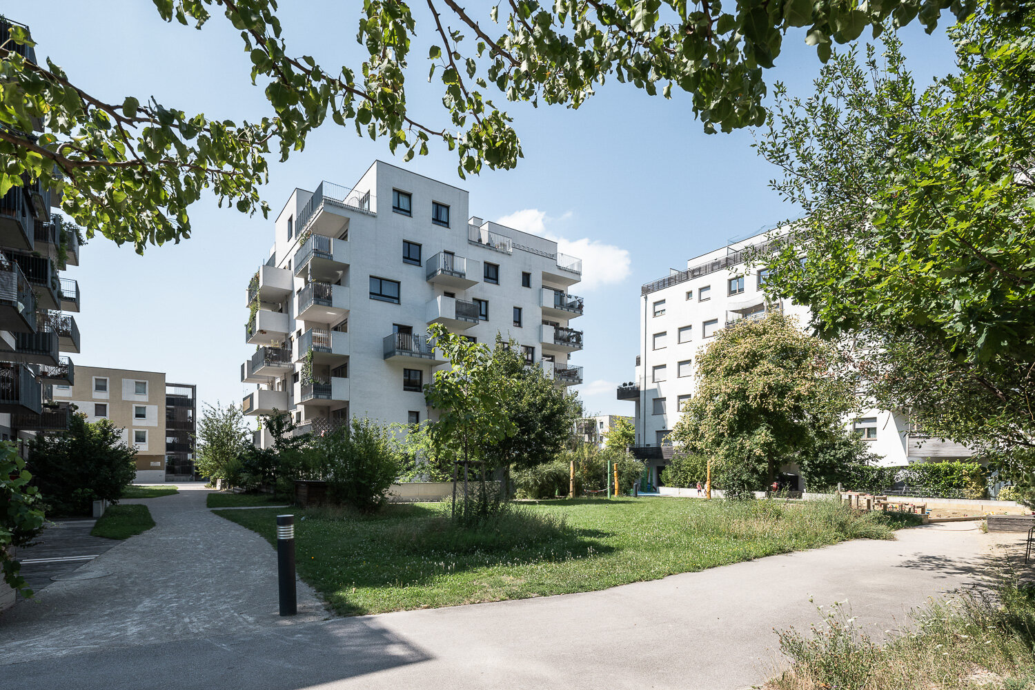 Sandspielplatz umgeben von Grünflächen und modernen Wohnhäusern an einem sonnigen Tag.