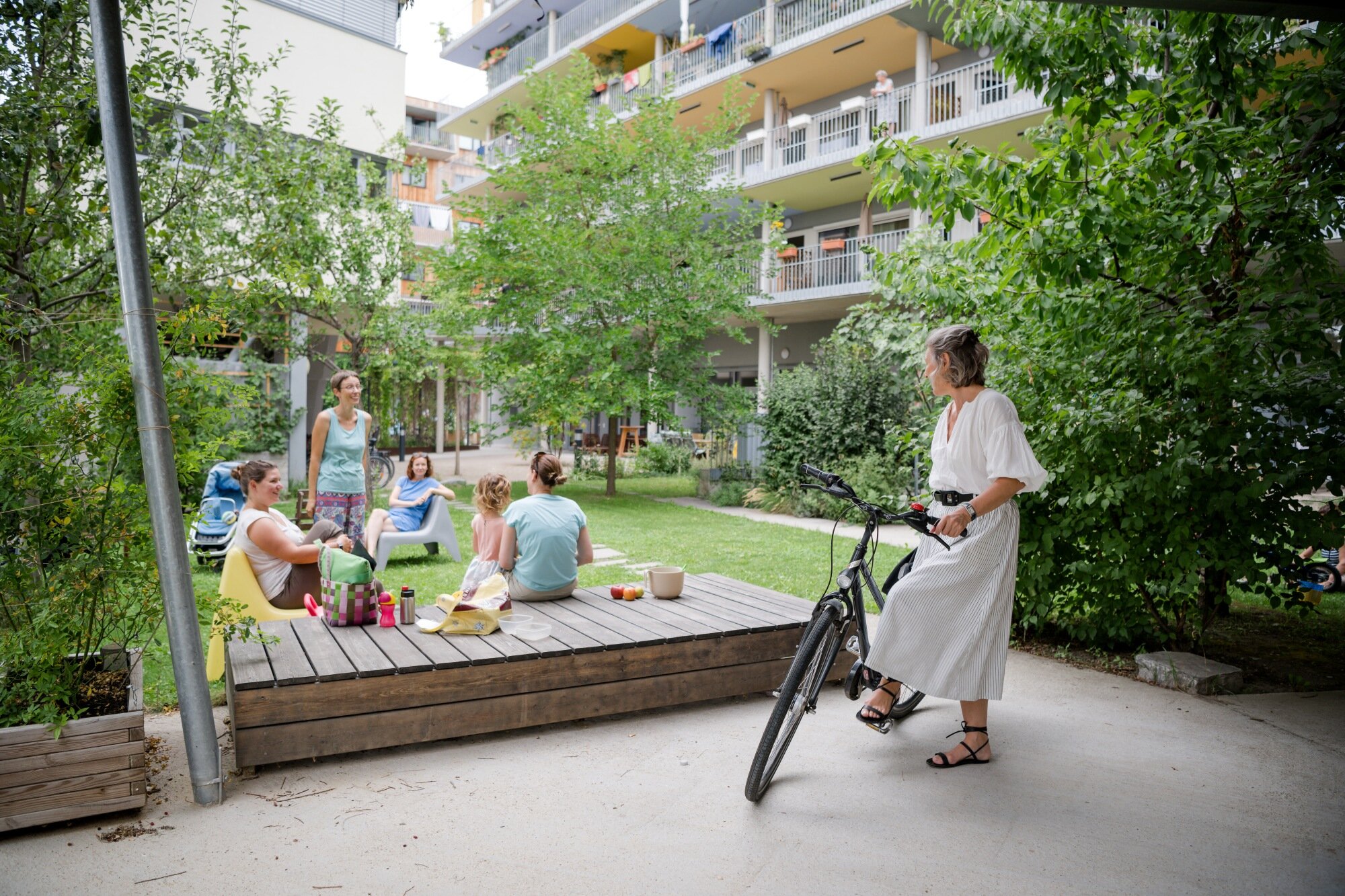Frauen und Kinder sitzen in einem sehr grünen Innenhof einer Baugruppe