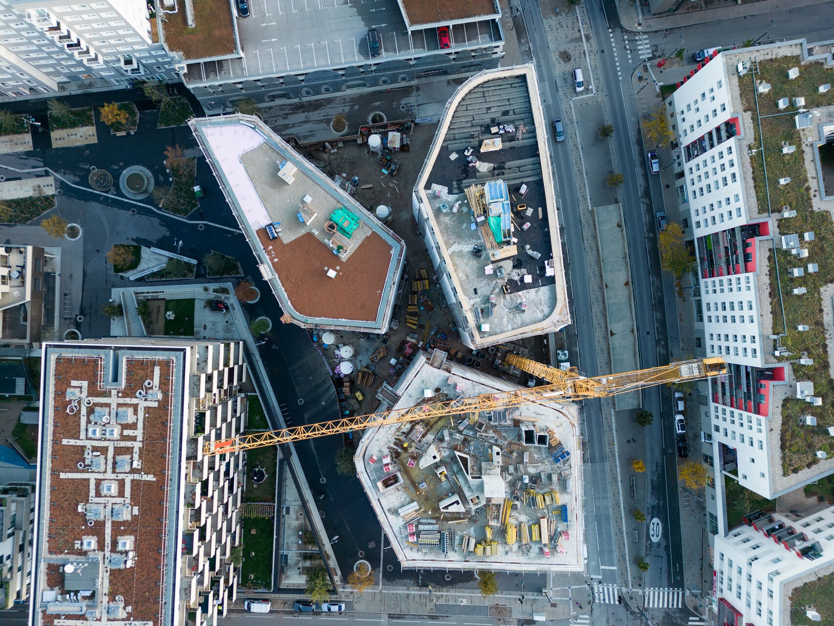 Aus der Vogrlperspektive: Hausdächer, die noch nicht fertig sind sowie ein Kran, dazwischen Straßen mit Autos