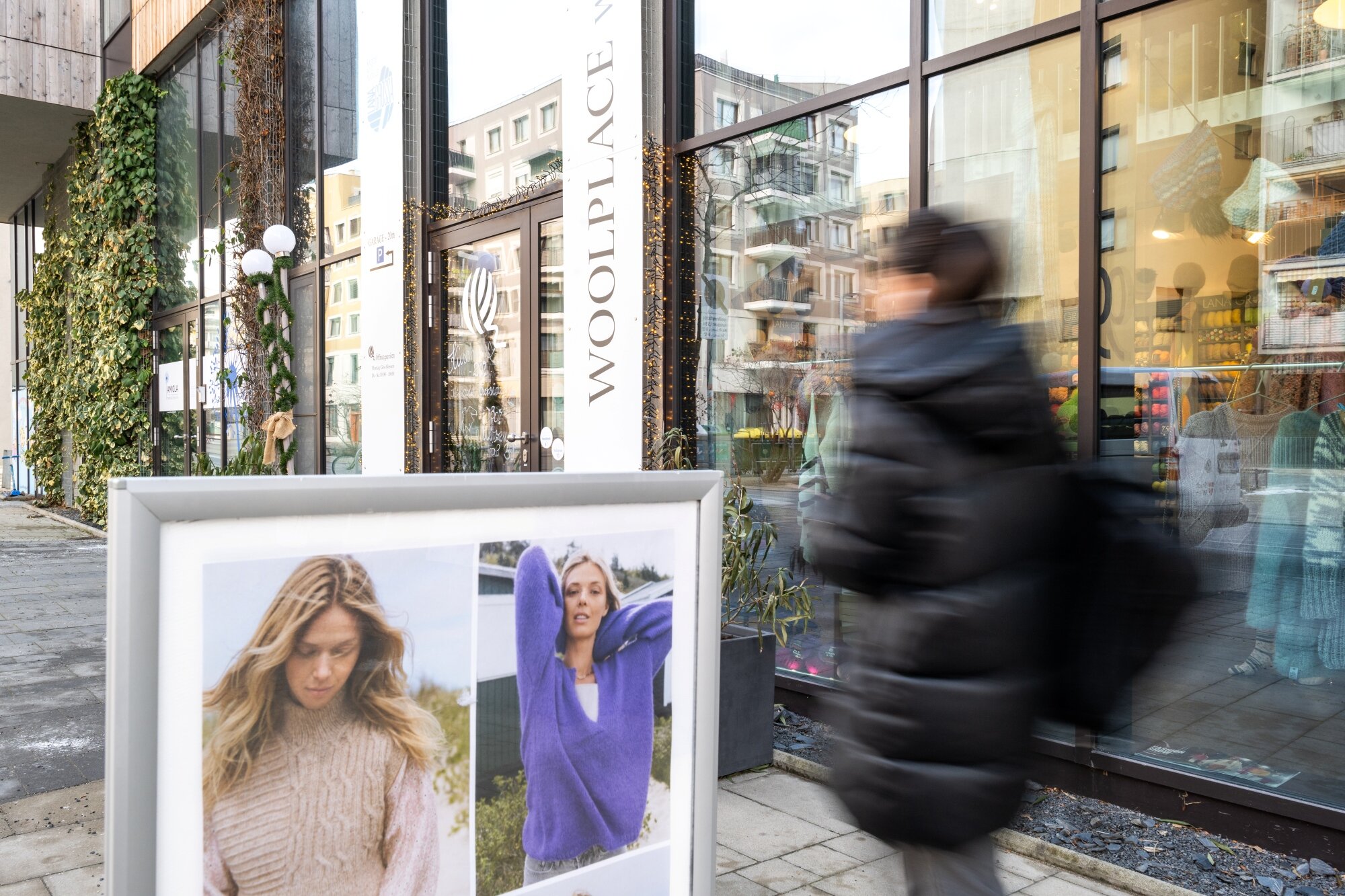 Frau geht an einem Fachgeschäft mit großen Auslagenfensten in einer Einkaufsstraße vorbei