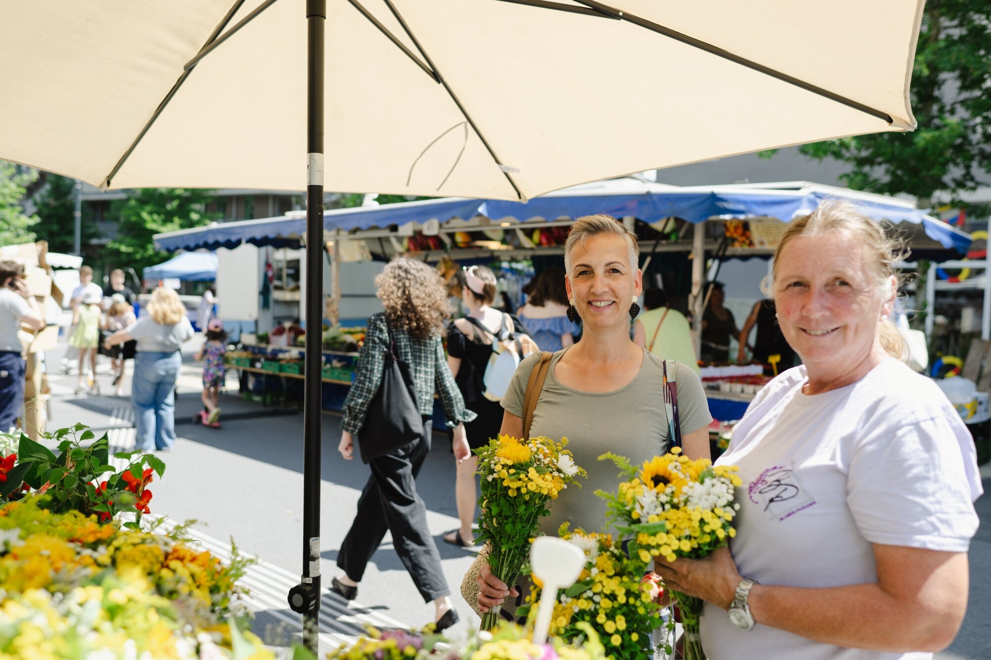Frauen stehen unter einem Sonnenschirm an einem Blumenstand am Markt in der Fußgängerzone mit vielen Besuchern