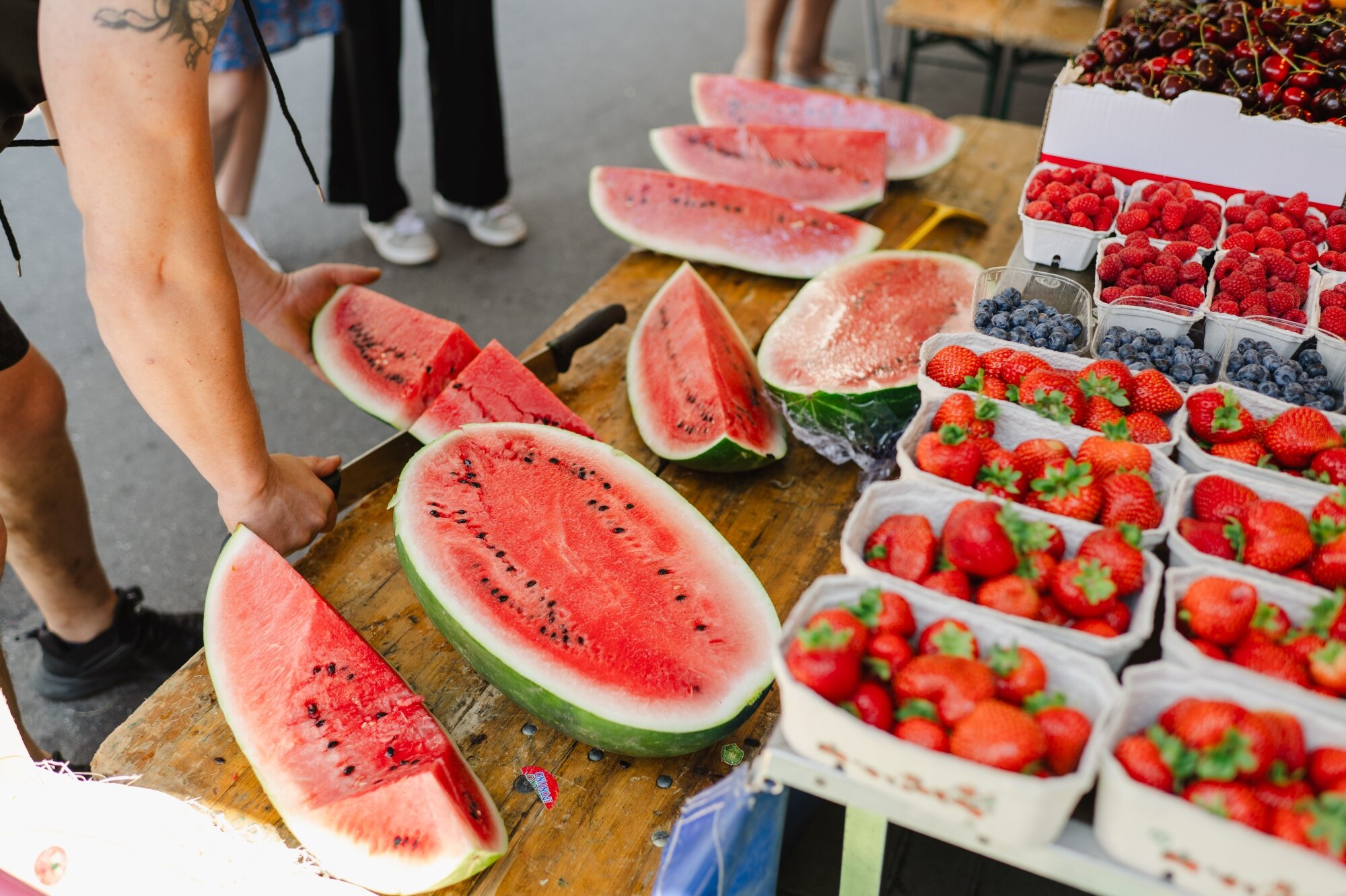frisches Obst am Mazzucco Markt Markthändler schneidet frische Wassermelone vor mehreren Tassen mit Erdbeeren