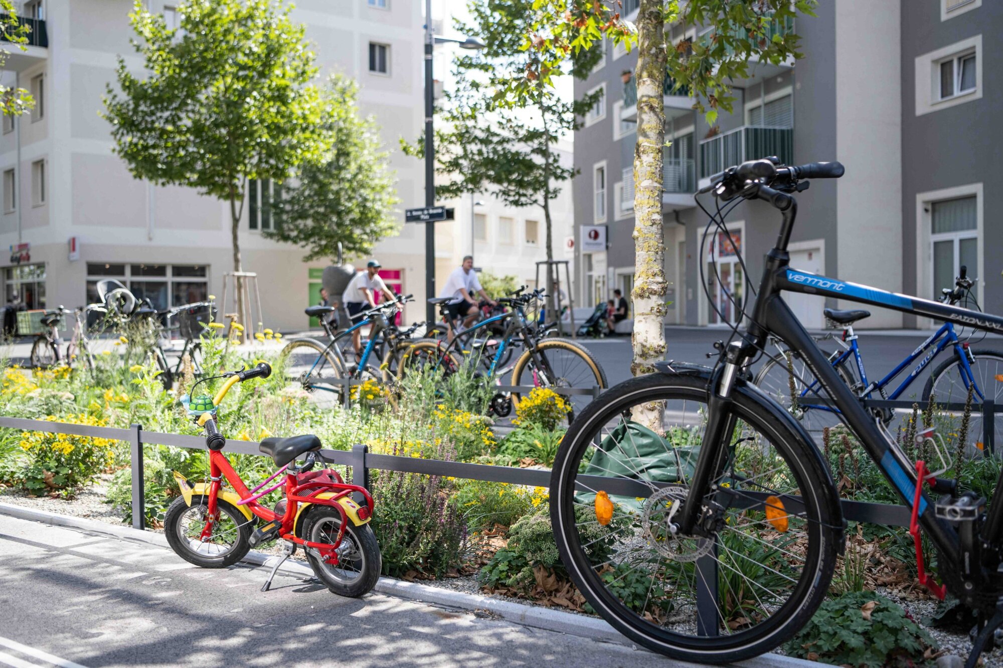 ein urbaner Platz mit Bäumen, Radfahrern und vielen Rädern