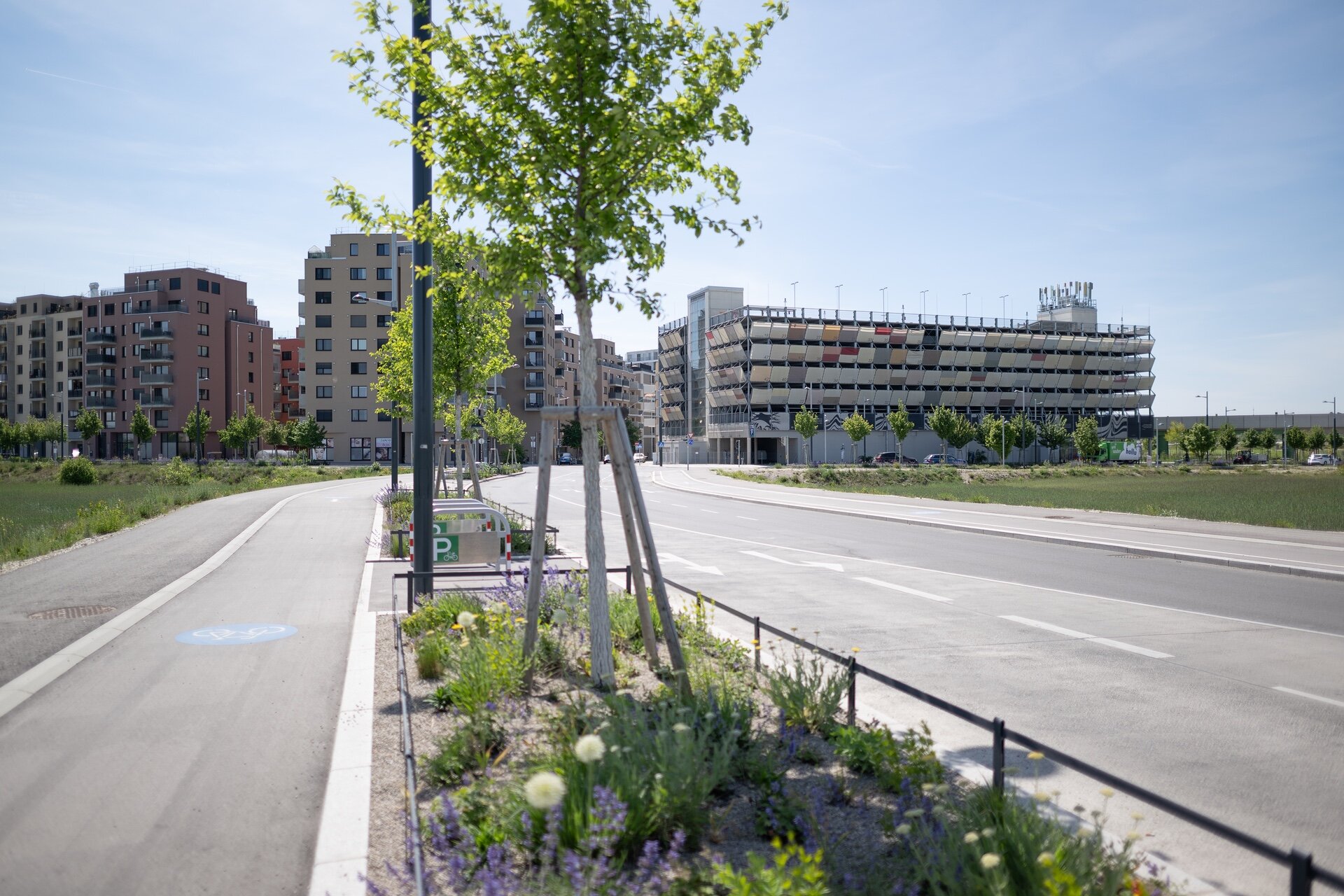 Blick auf die VHS Kulturgarage in der Seestadt Wien mit angrenzenden Wohngebäuden und begrünten Straßen – Sammelgarage als Teil des nachhaltigen Mobilitätskonzepts.