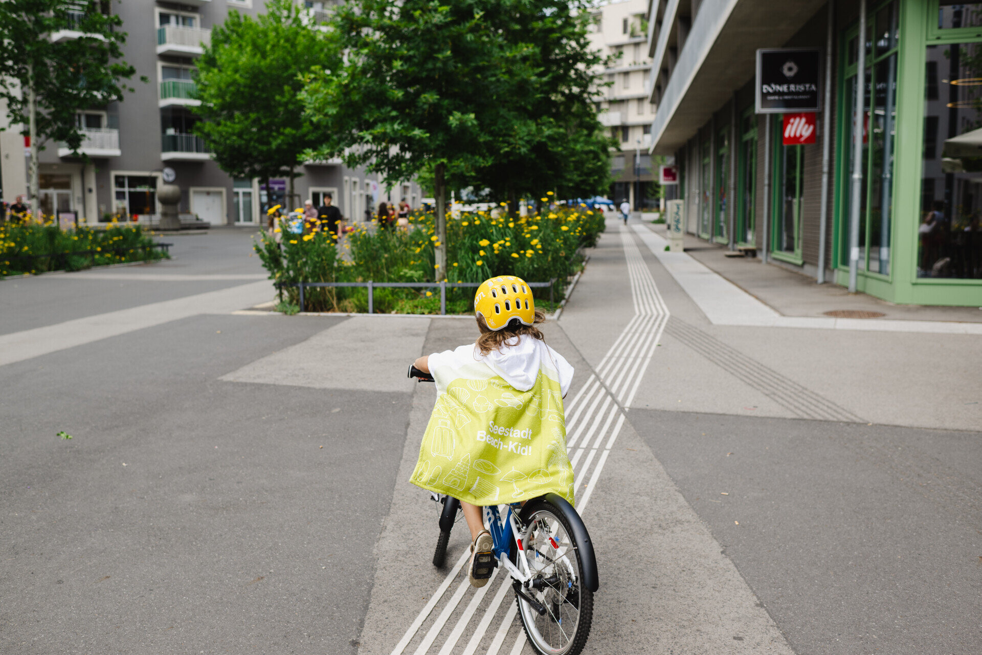 Kind mit Fahrrad und Helm fährt durch eine autofreie Straße in der Seestadt Wien – sicheres Umfeld mit viel Platz für nachhaltige Mobilität und Alltag im Quartier.