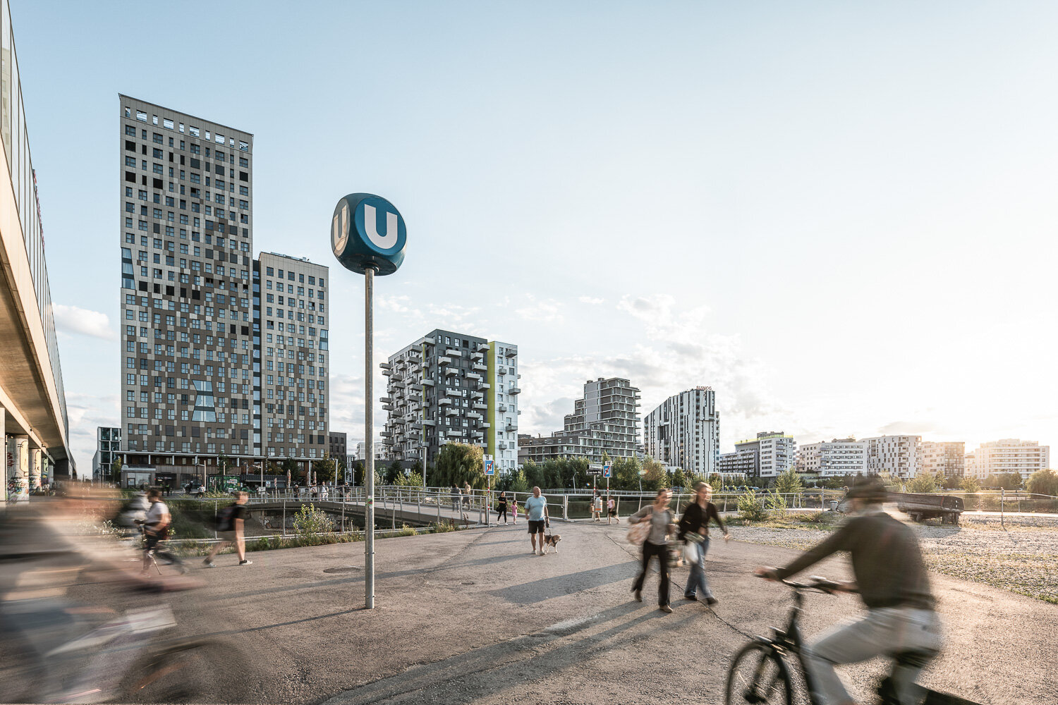Mobilität in der Seestadt Menschen zu Fuß und mit Rad fahren vor einer urbanen Skyline der Seestadt mit direkter U-Bahn Anbindung
