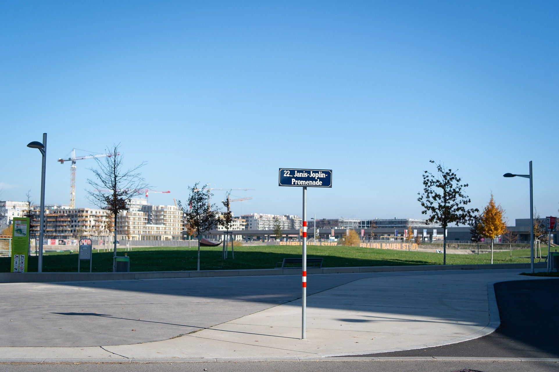 Straßenschild Janis-Joplin-Promenade, dahinter ein Park und dahinter Gebäude