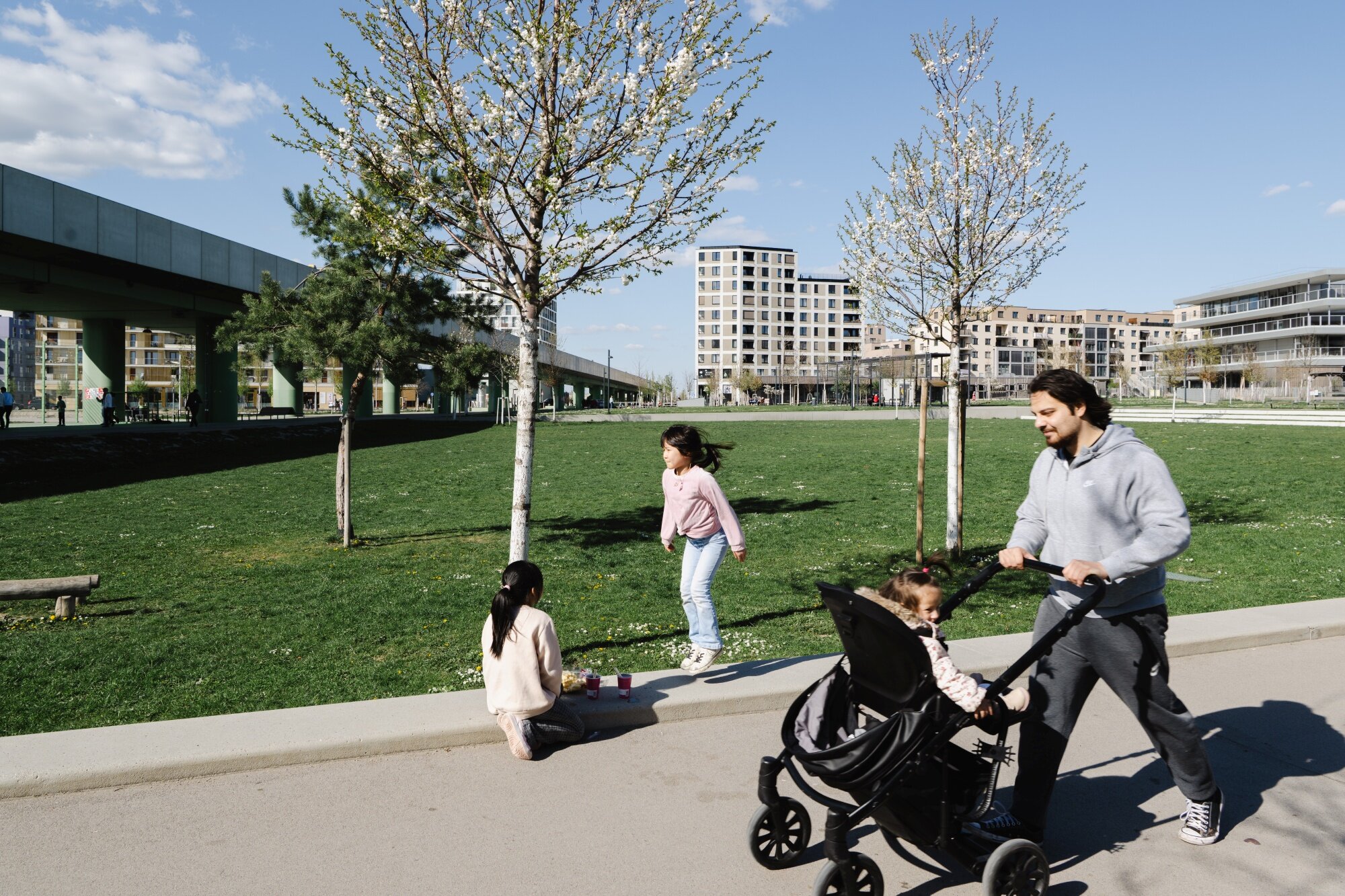 zentraler Park für viele Nutzungen im Quartier-Am-Seebogen Vater mit Kinderwagen und junge Mädchen am Fußgängerweg im Elinor-Ostrom-Park mit U-Bahn-Tresse im Hintergrund