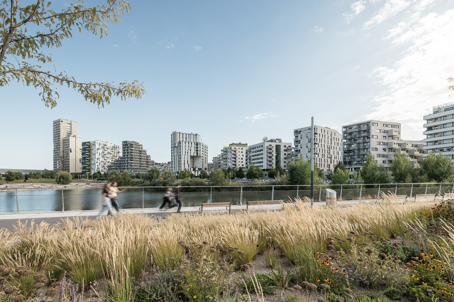 Menschen gehen entland der Seepromenade mit Blick auf die Skyline und den Seepark