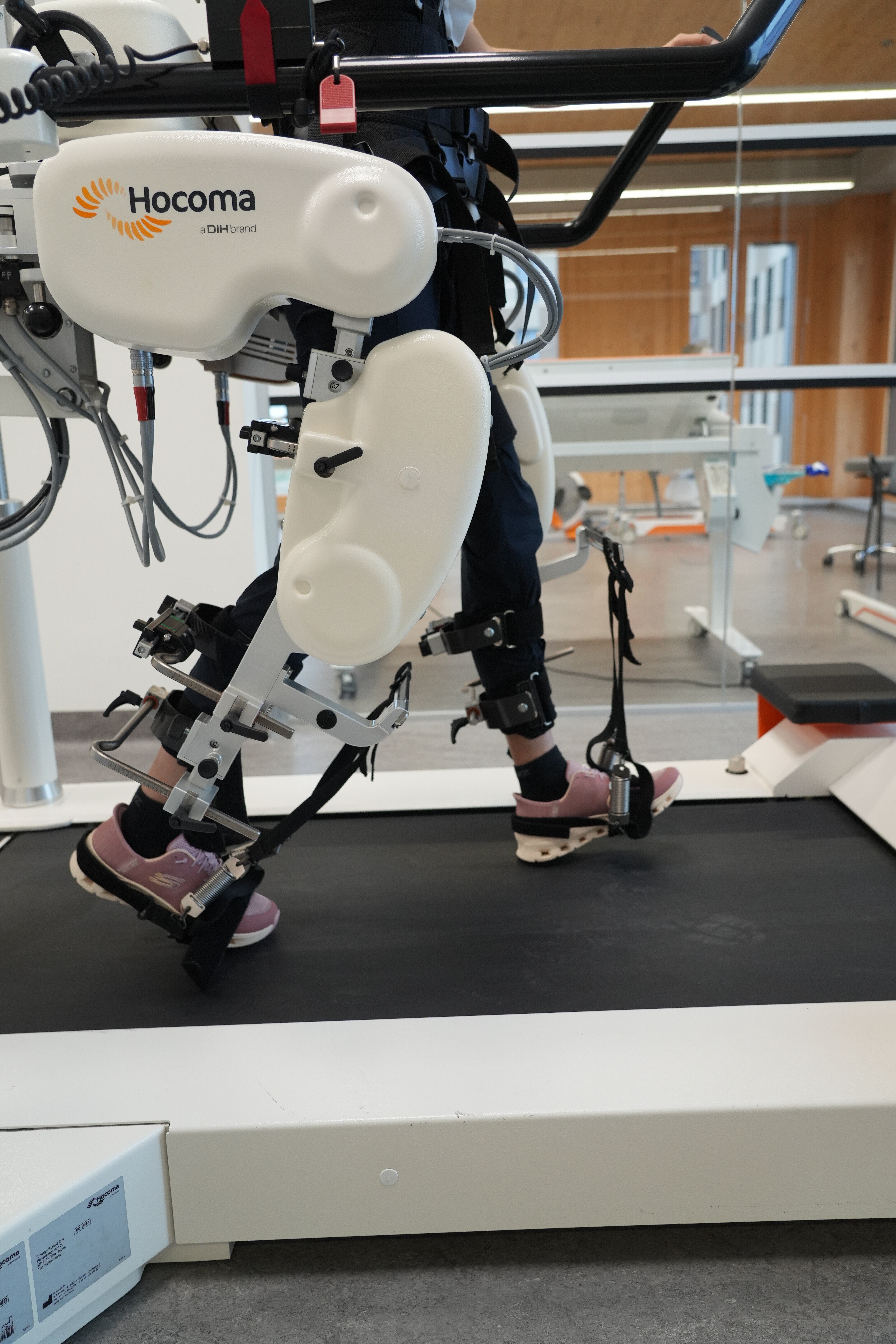 Auf einem Laufband bewegt sich eine Person in Laufschuhen, die Beine sind in ein Therapiegerät eingespannt