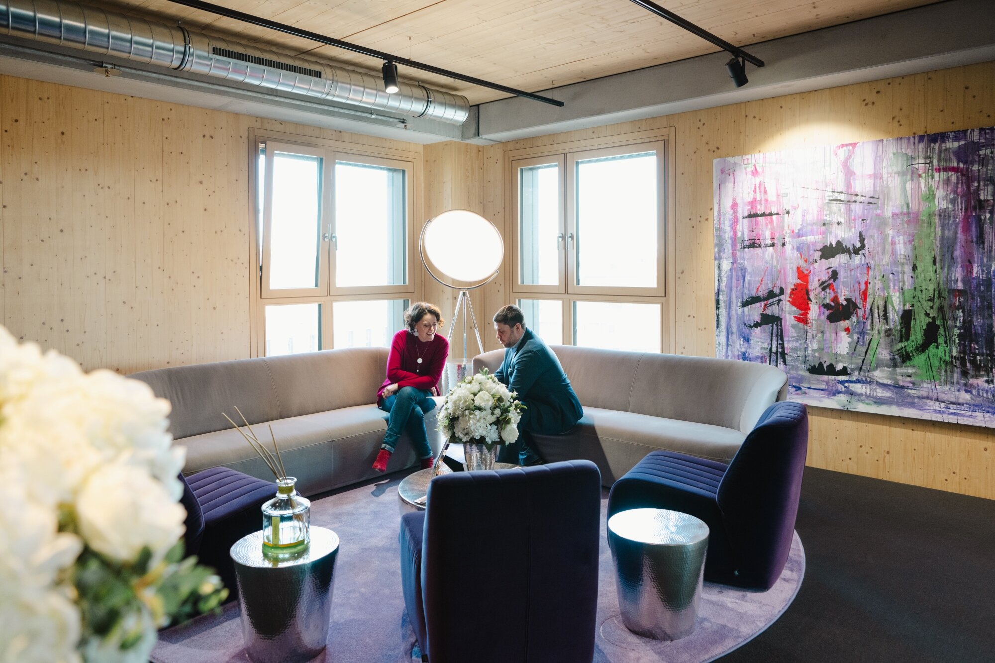 Faru und Mann sitzen in einem Meetingraum mit Holzwänden, Kunst an der Wand und exklusiven Loungemöbeln