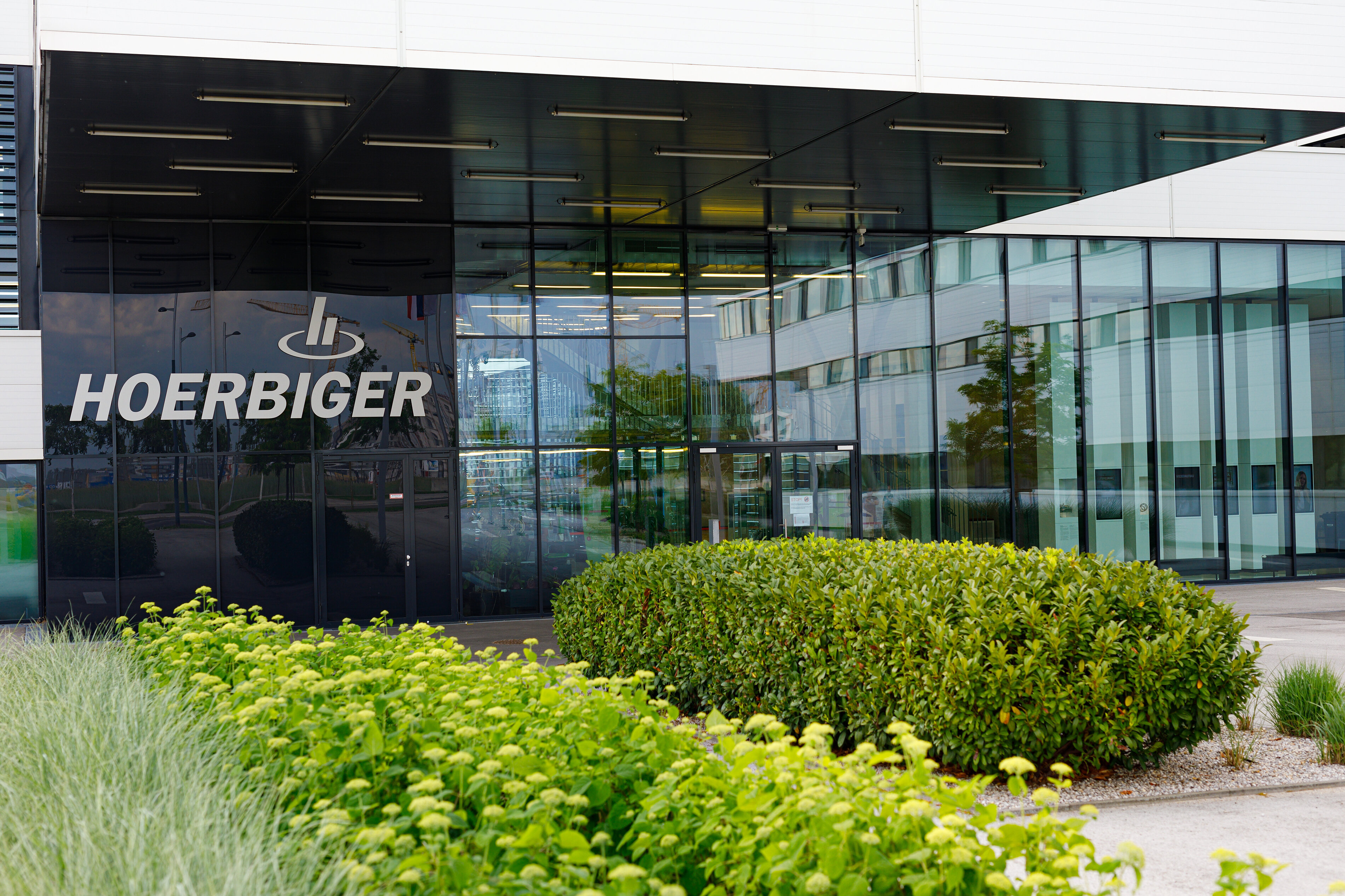 stark begünter Eingang zum modernen verglasten Hauptgebäude von Hörbiger in der Seestadt