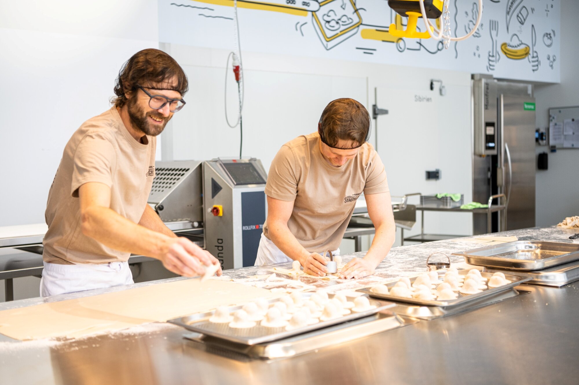 zwei junge Männer mit Haarnetz machen original Kärntner Kasnudln in einer hellen Produktionshalle