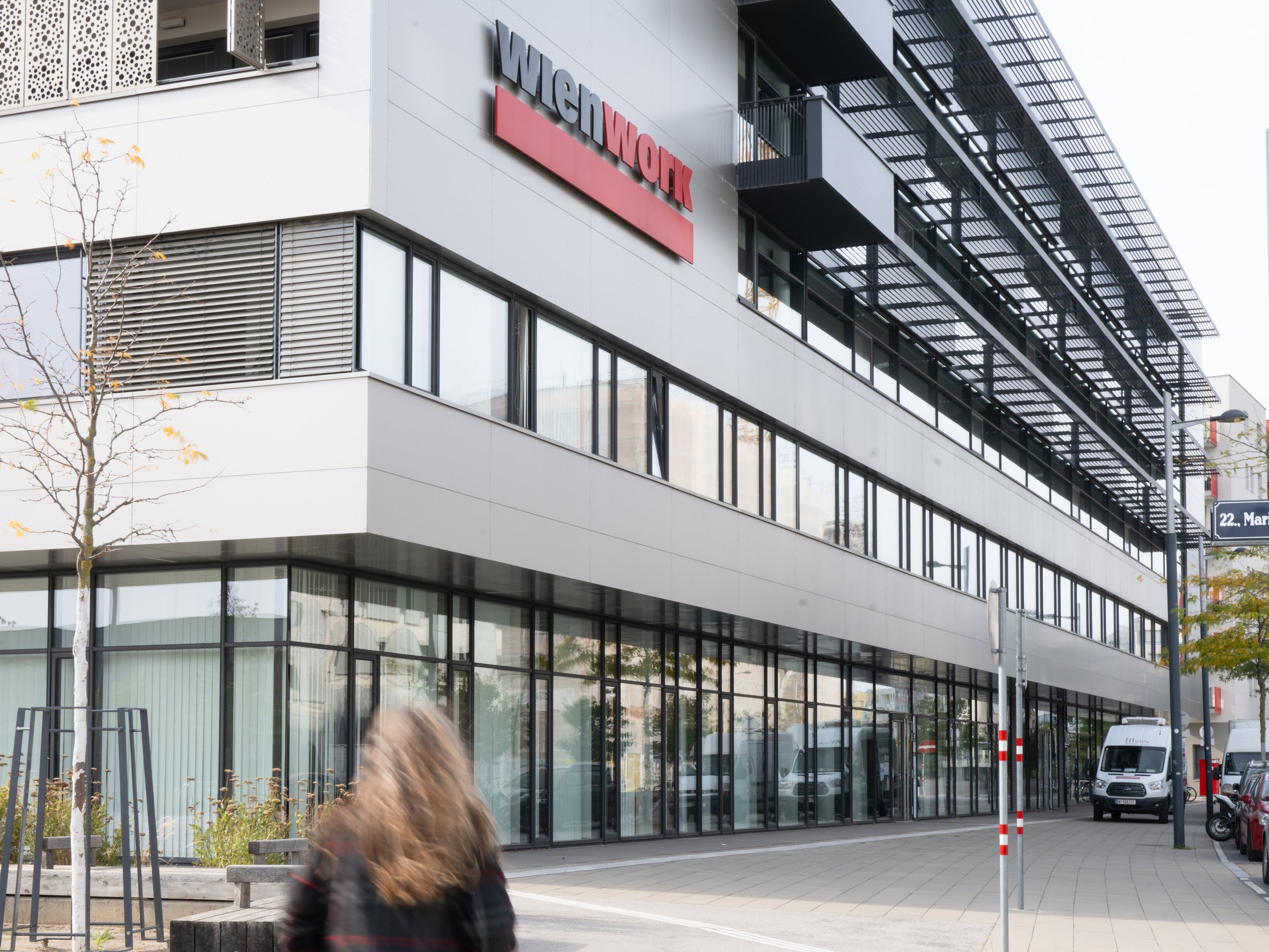 Frau geht einen breiten Gehsteig entlang vor einem modernen Gebäude mit der Aufschrift wienwork