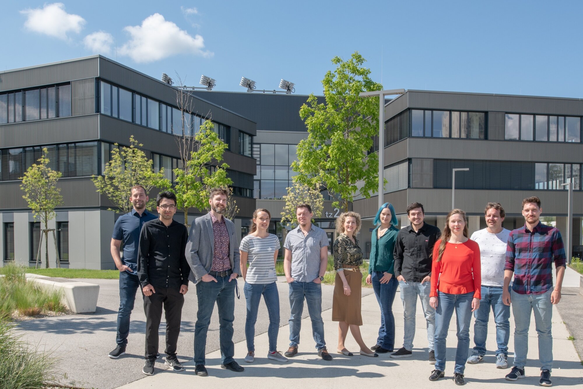 mehrere Menschen vom Team von incus stehen bei Sonnenschein vor einem modernen Gewerbegebäude mit mehreren Bäumen